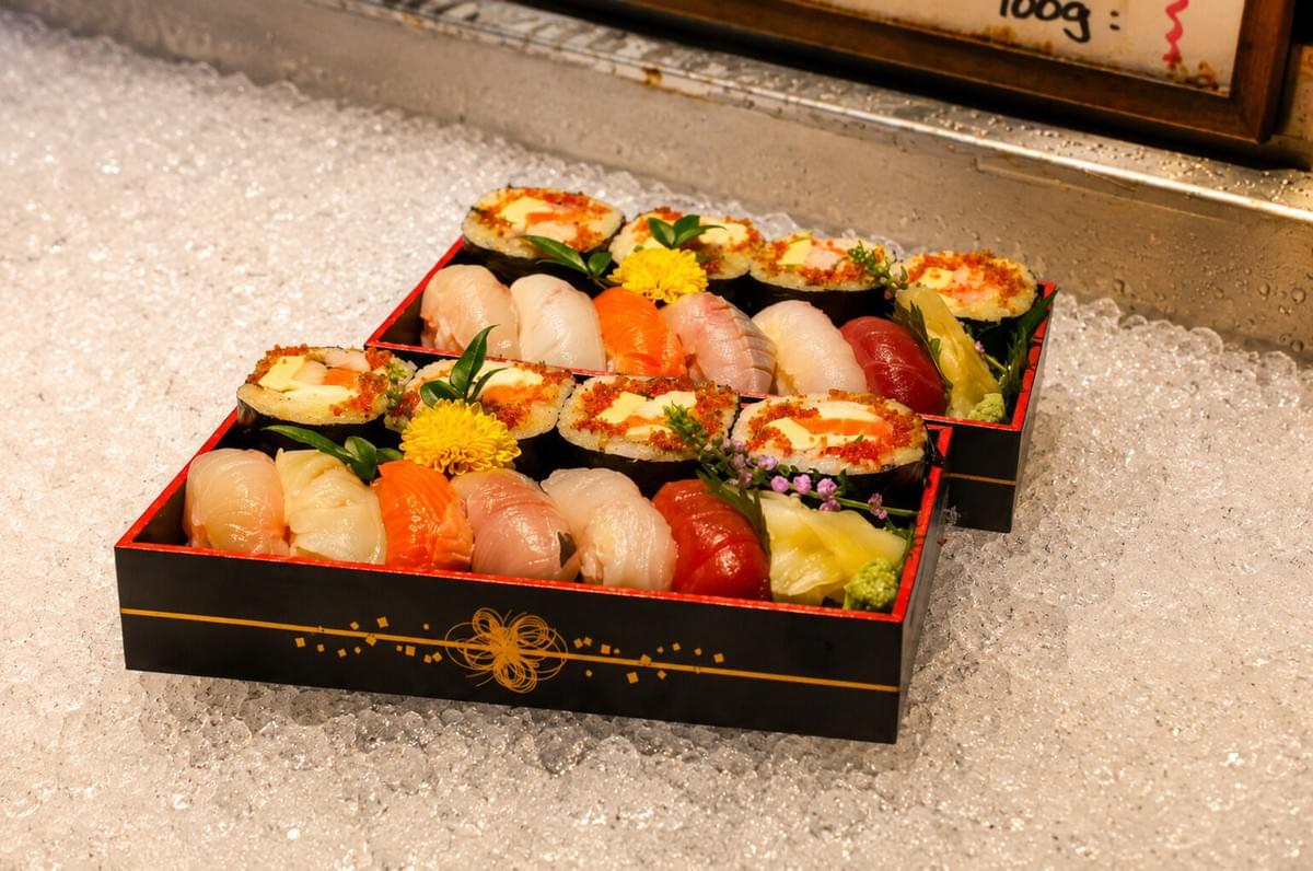Two black bento boxes of sushi and maki rolls resting on crushed ice. Two black bento boxes of sushi and maki rolls resting on crushed ice.