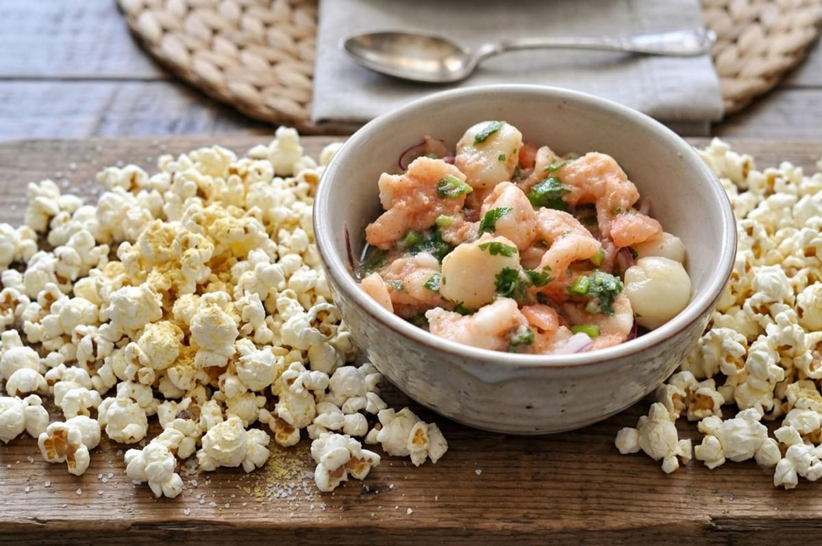 Rustic bowl of Ecuadorian ceviche with corn served on a wooden board, surrounded by scattered popcorn kernels Rustic bowl of Ecuadorian ceviche with corn served on a wooden board, surrounded by scattered popcorn kernels