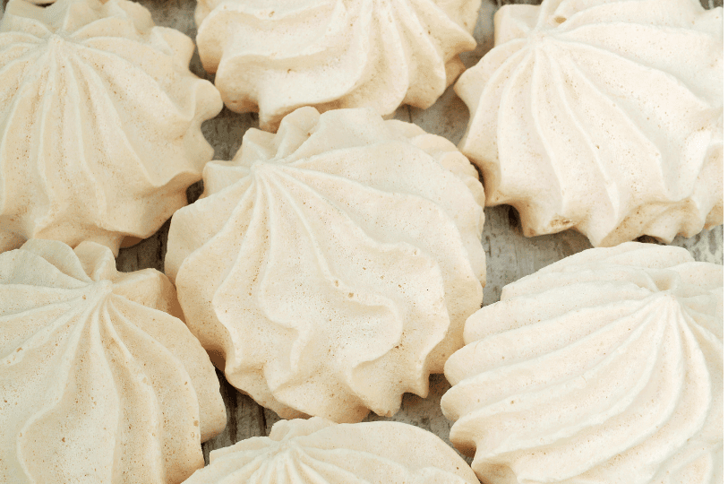 high-angle, close-up view of several cream-colored meringue cookies resting on a rustic wooden surface, showcasing the swirling patterns created by a star piping tip. high-angle, close-up view of several cream-colored meringue cookies resting on a rustic wooden surface, showcasing the swirling patterns created by a star piping tip.