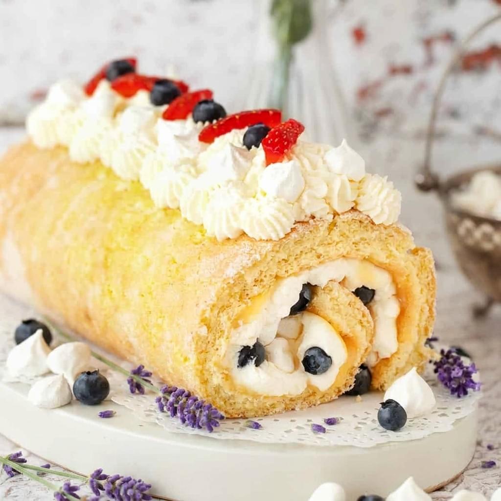 A long meringue pavlova roll filled with cream and strawberries sitting on a dark serving platter, with a hand using a long kitchen knife to cut it into slices. A long meringue pavlova roll filled with cream and strawberries sitting on a dark serving platter, with a hand using a long kitchen knife to cut it into slices.