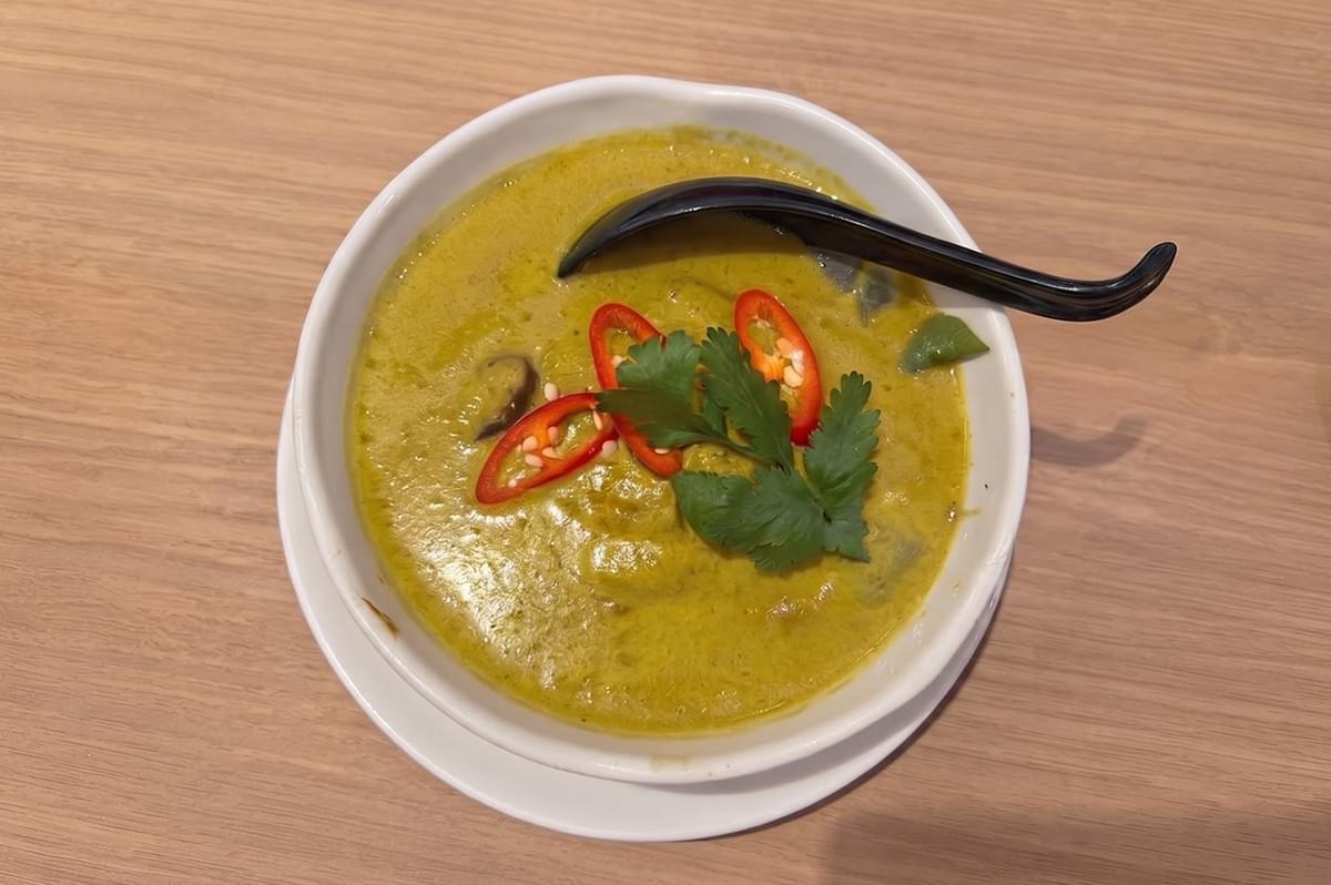 Bowl of Thai green curry chicken garnished with sliced red chili peppers and fresh cilantro. Bowl of Thai green curry chicken garnished with sliced red chili peppers and fresh cilantro.