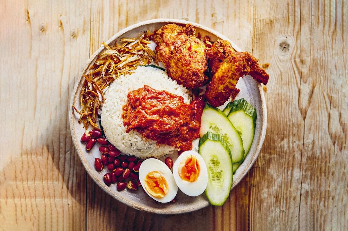 A plate of nasi lemak with rice, fried chicken, sambal, anchovies, peanuts, cucumber, and boiled eggs. A plate of nasi lemak with rice, fried chicken, sambal, anchovies, peanuts, cucumber, and boiled eggs.