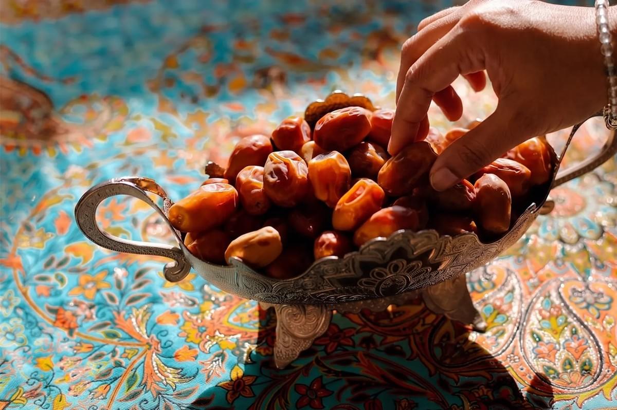 Hand reaching for fresh organic dates in a decorative silver bowl. Hand reaching for fresh organic dates in a decorative silver bowl.
