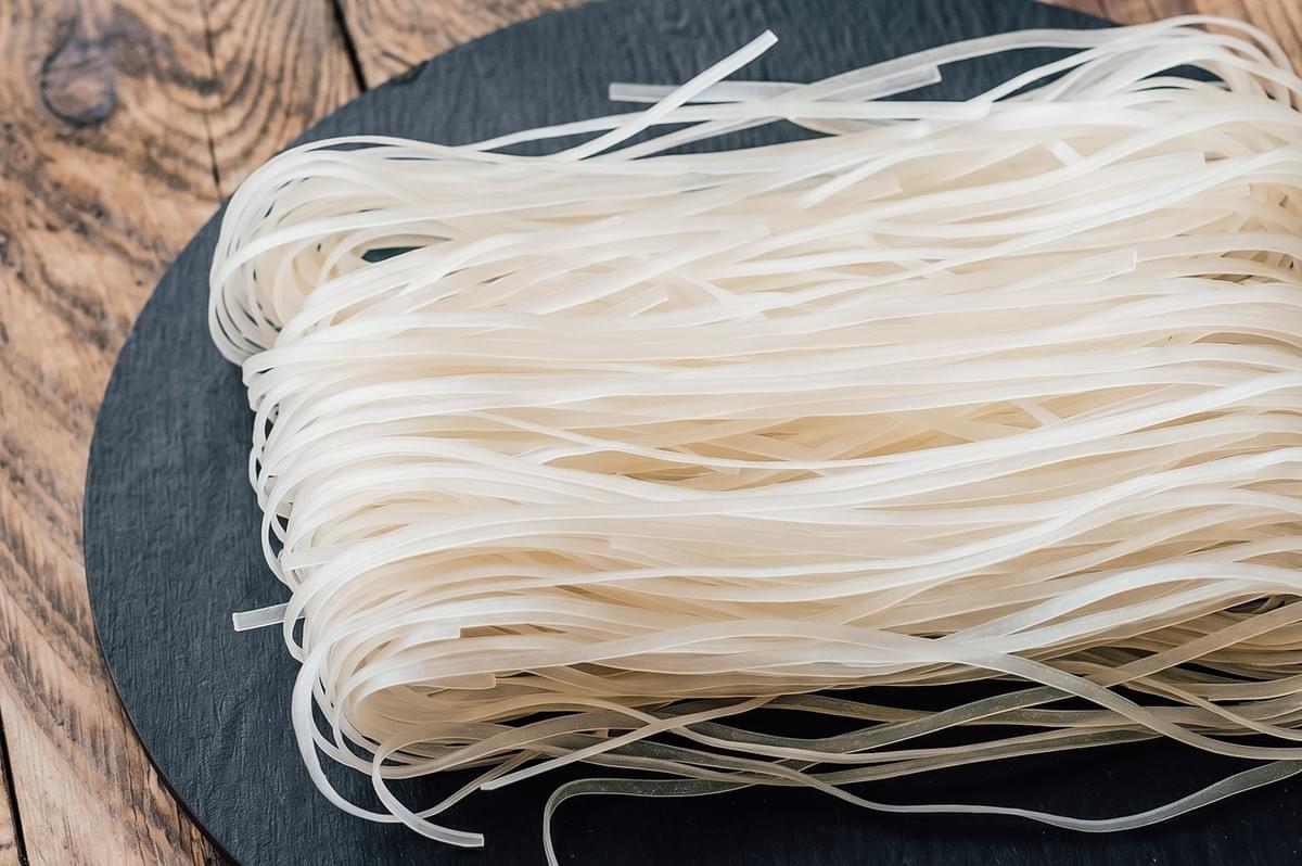 Close-up top-down shot of dry rice noodles on a dark plate, the essential base ingredient for authentic pad thai recipe and traditional Thai stir-fried noodle dishes. Close-up top-down shot of dry rice noodles on a dark plate, the essential base ingredient for authentic pad thai recipe and traditional Thai stir-fried noodle dishes.
