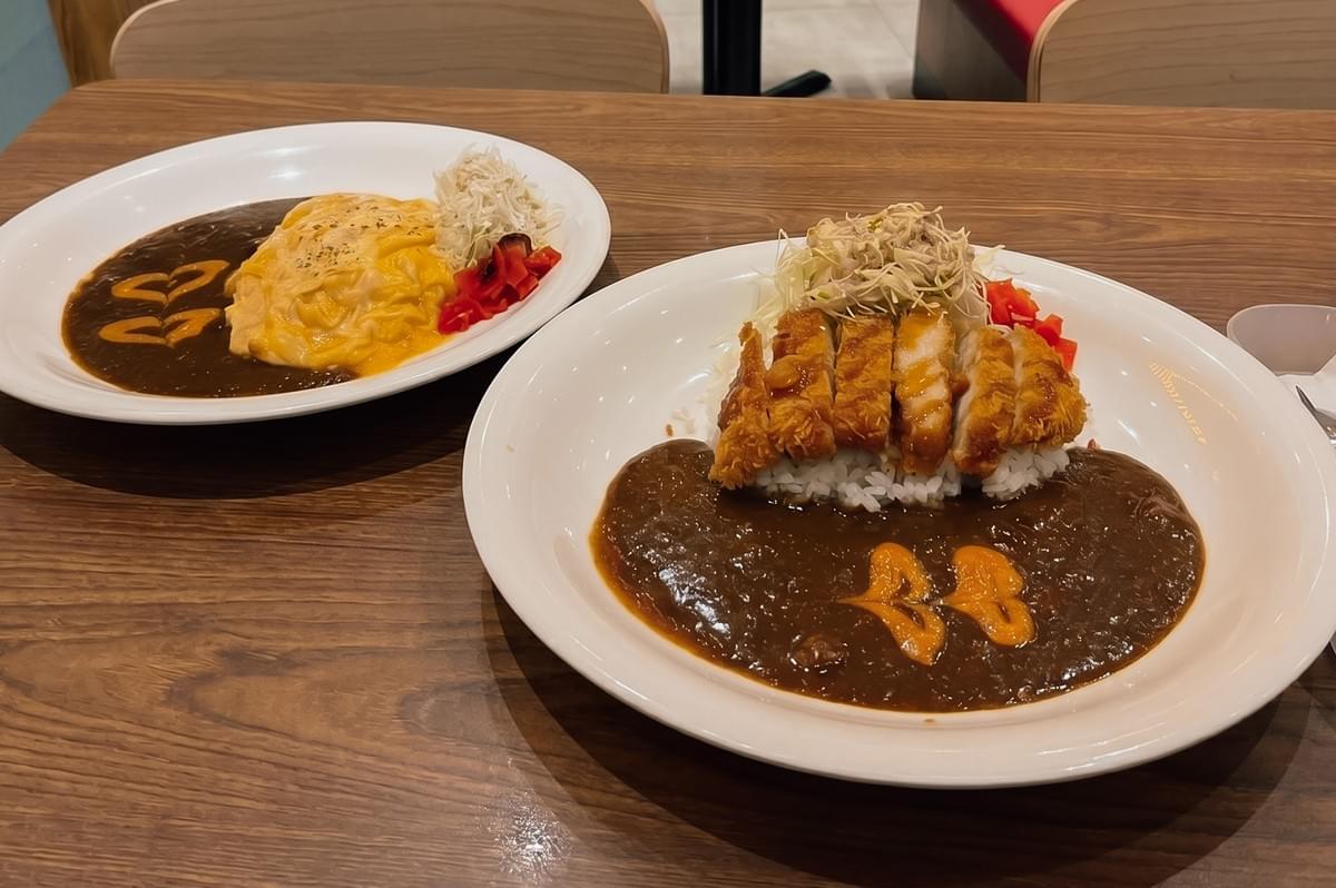 Slight high-angle medium shot of chicken katsu curry and omurice curry dishes at Monster Curry Jewel Changi Airport, served with rice, thick Japanese curry sauce, and shredded cabbage. Slight high-angle medium shot of chicken katsu curry and omurice curry dishes at Monster Curry Jewel Changi Airport, served with rice, thick Japanese curry sauce, and shredded cabbage.