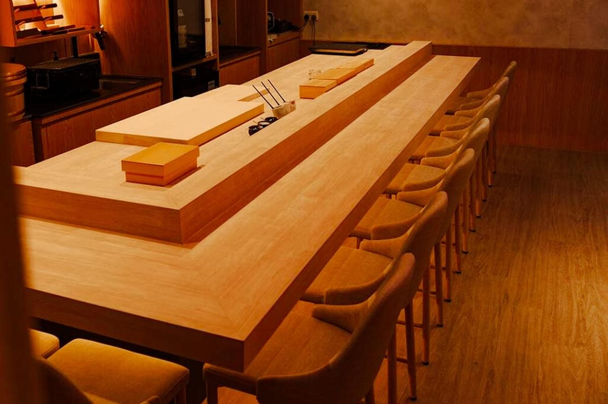 Minimalist omakase restaurant interior featuring a long wooden sushi counter, soft warm lighting, and neatly arranged seating. Minimalist omakase restaurant interior featuring a long wooden sushi counter, soft warm lighting, and neatly arranged seating.