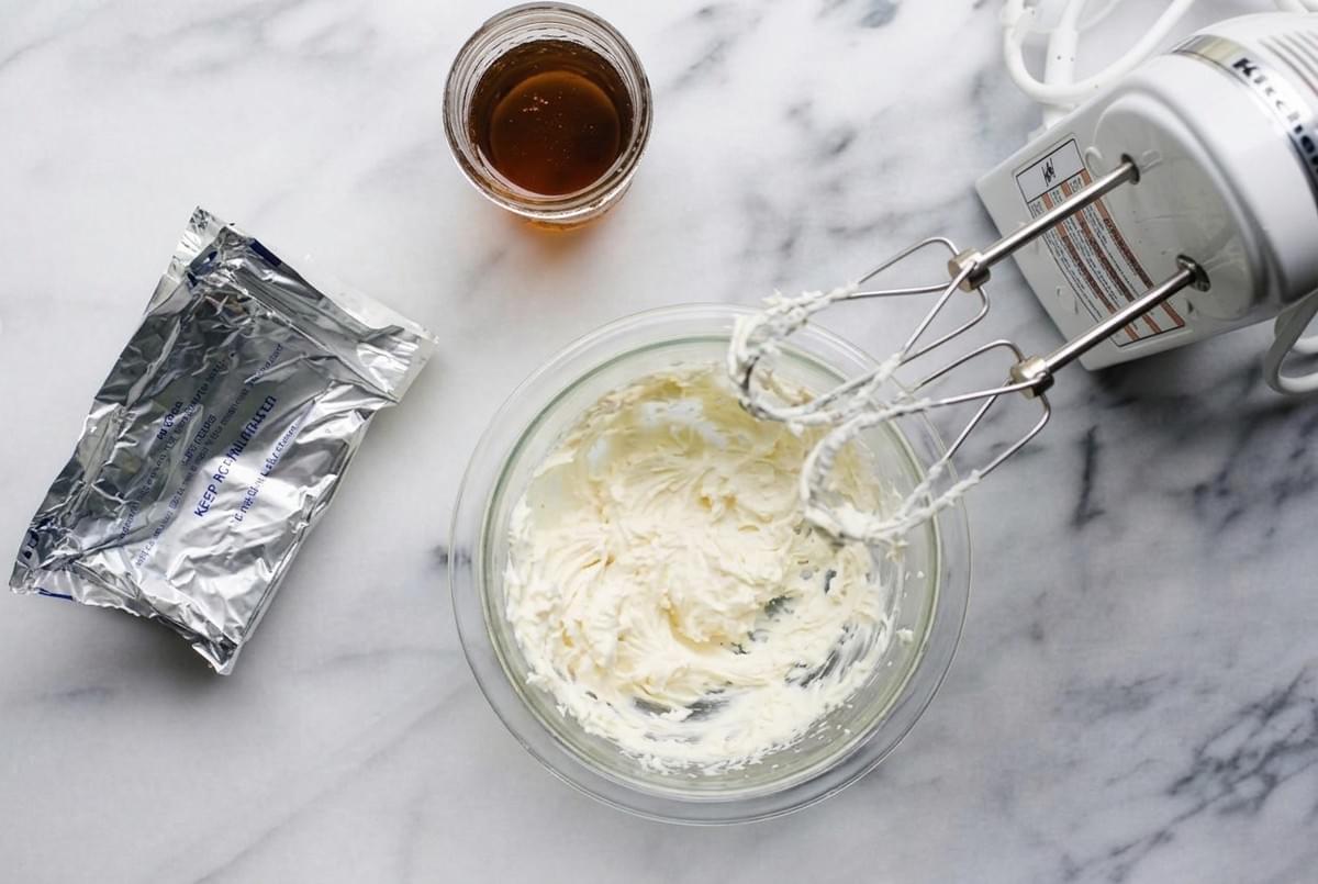 Whipping cream cheese filling in a glass bowl using an electric hand mixer on marble. Whipping cream cheese filling in a glass bowl using an electric hand mixer on marble.