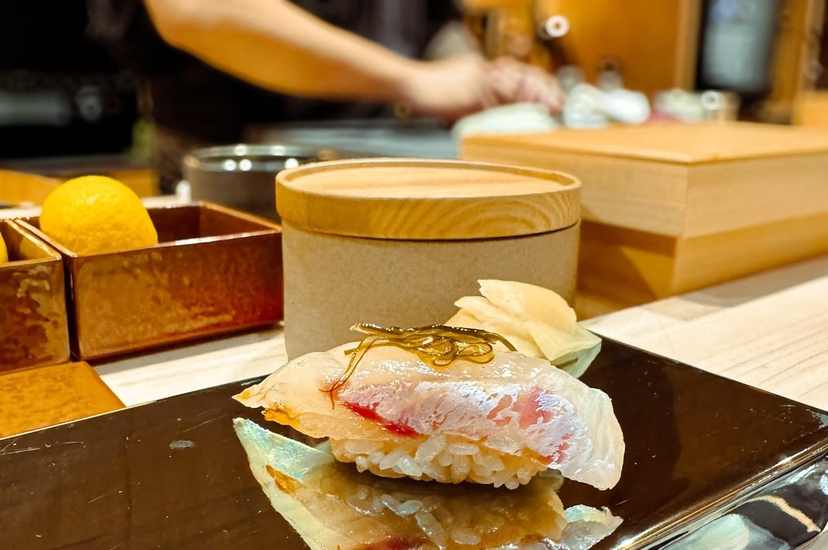 Close-up of fresh sushi served on a reflective plate, with delicate garnishes and traditional omakase tableware in the background. Close-up of fresh sushi served on a reflective plate, with delicate garnishes and traditional omakase tableware in the background.