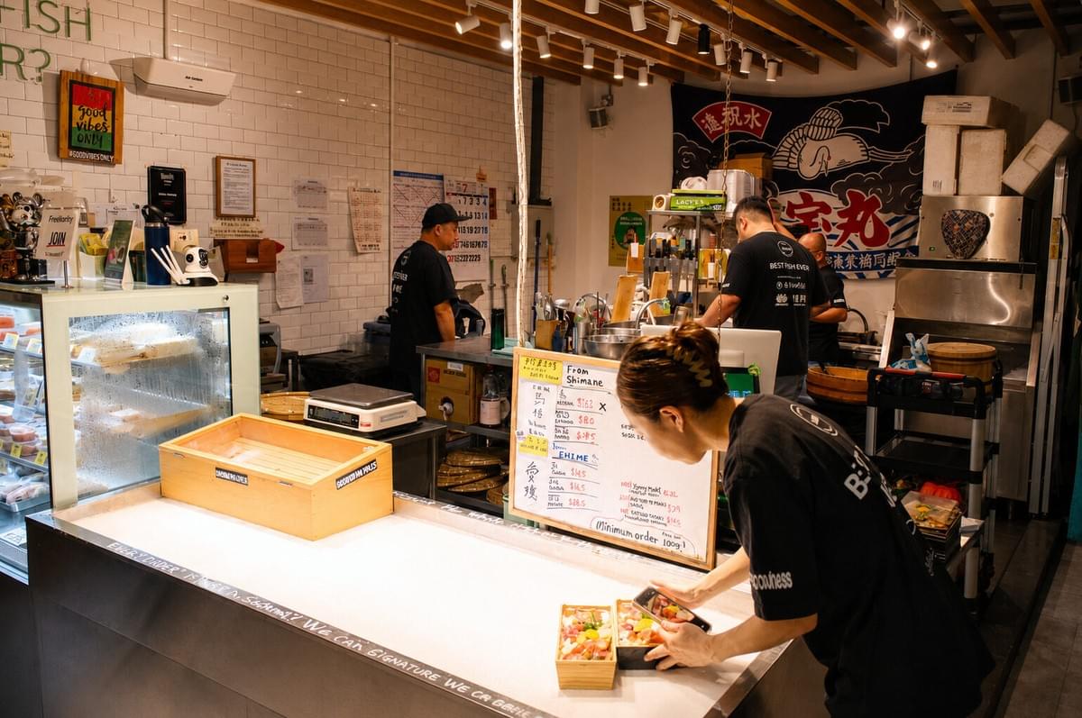 Seafood counter staff member taking a photo of two freshly prepared sushi bento boxes. Seafood counter staff member taking a photo of two freshly prepared sushi bento boxes.