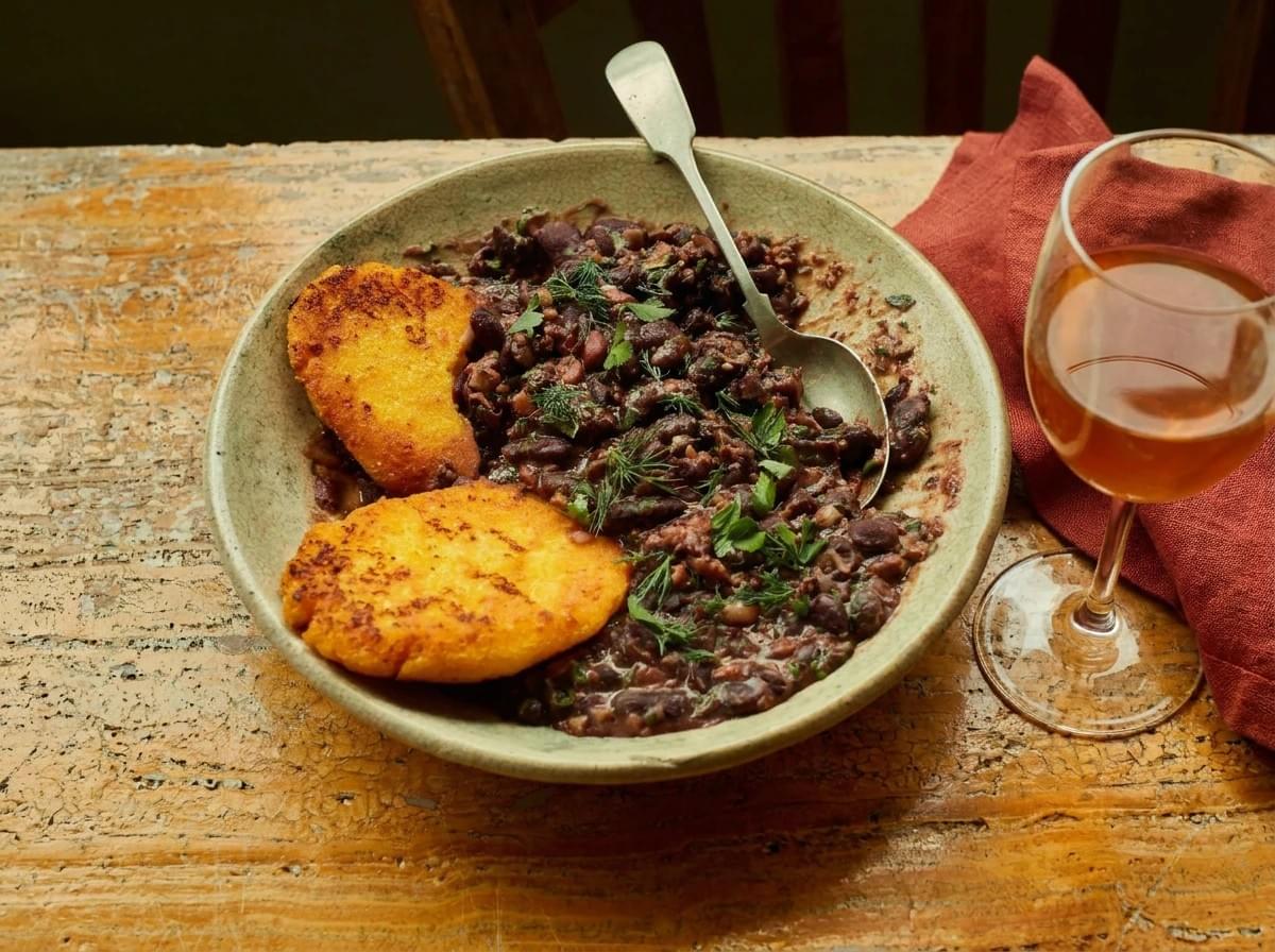 Ceramic plate with stewed red beans, golden fried cornbread patties, and a glass of amber wine. Ceramic plate with stewed red beans, golden fried cornbread patties, and a glass of amber wine.
