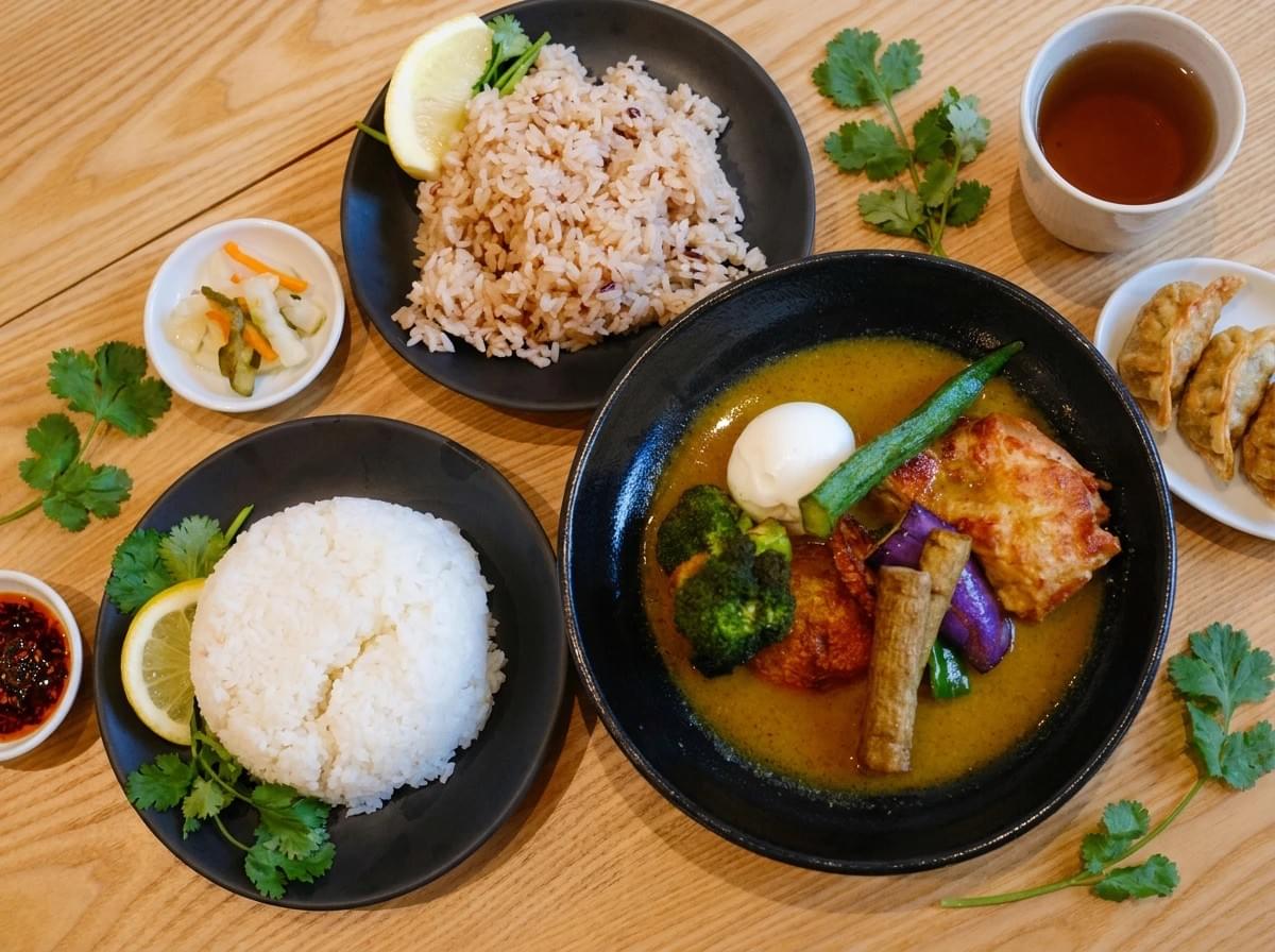 Flat-lay view of a Japanese soup curry meal set with white rice, grain rice, fried dumplings, tea, and pickles. Flat-lay view of a Japanese soup curry meal set with white rice, grain rice, fried dumplings, tea, and pickles.