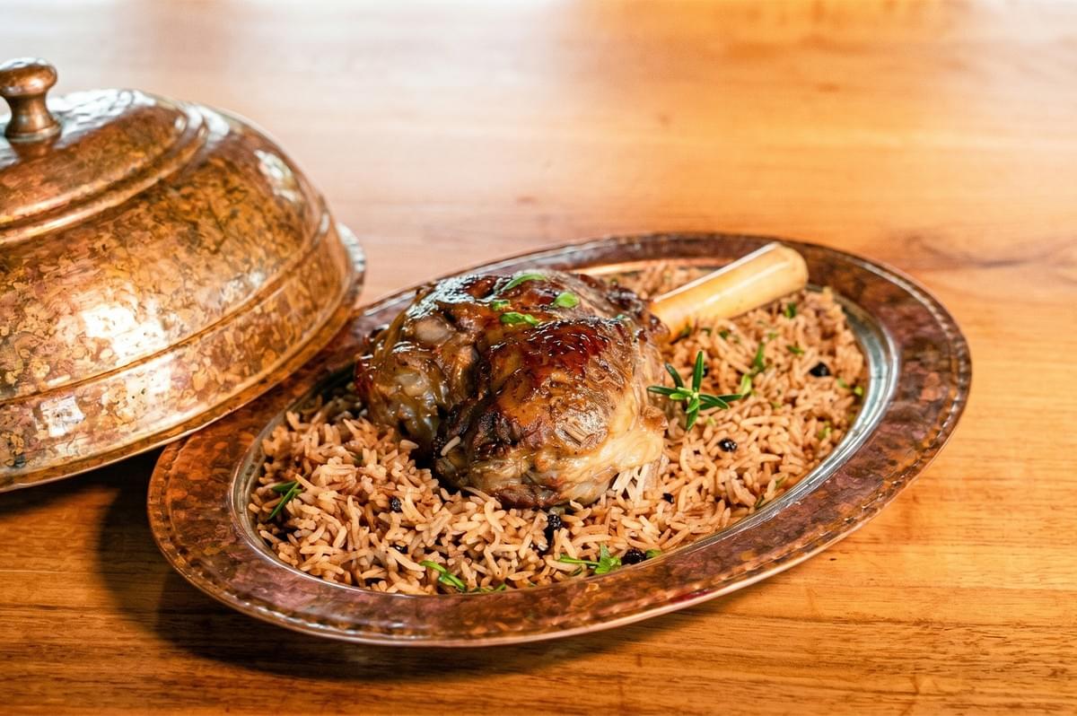 Roasted lamb shank served over spiced basmati rice on a traditional copper platter. Roasted lamb shank served over spiced basmati rice on a traditional copper platter.
