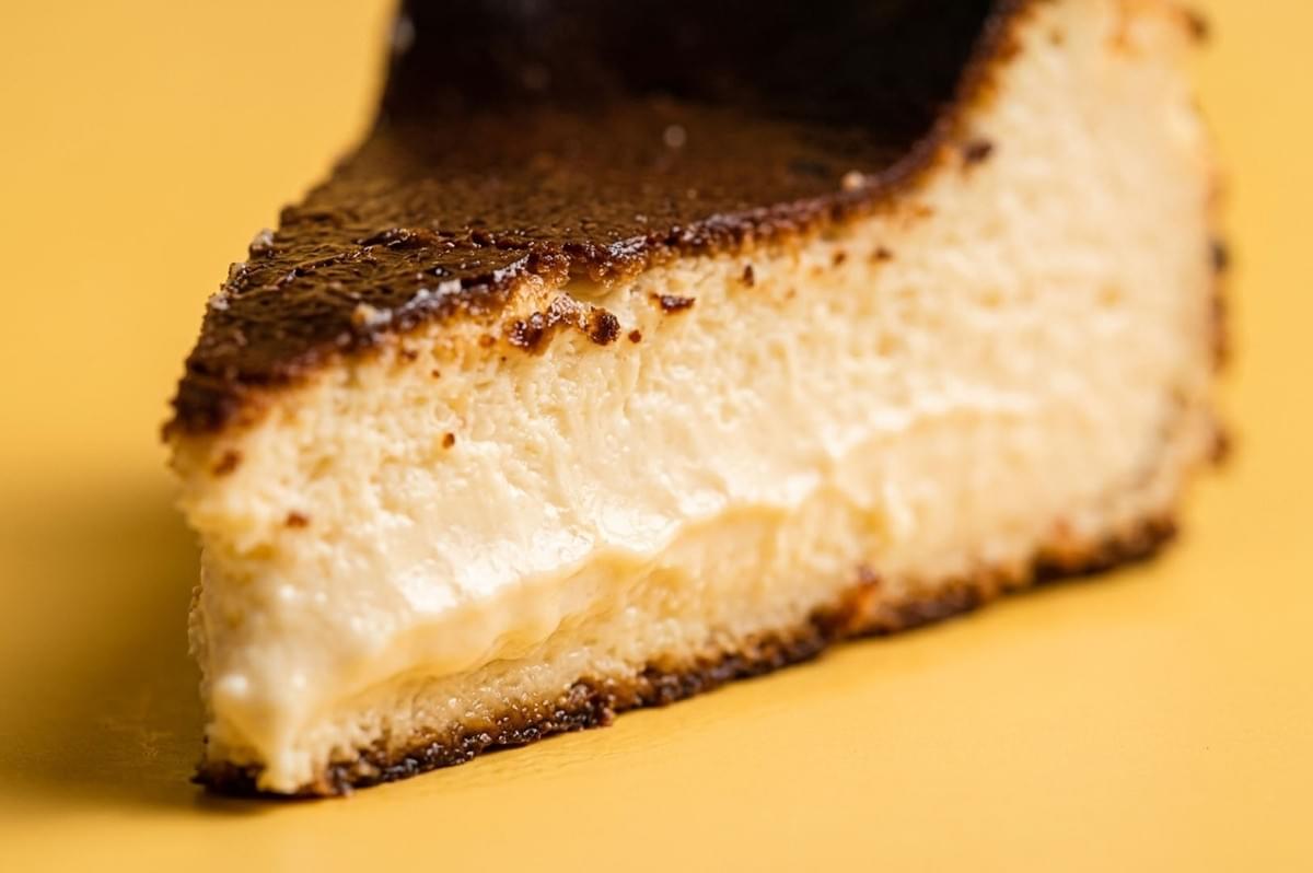 Close-up slice of Basque burnt cheesecake showing creamy interior and deeply caramelized top on yellow background Close-up slice of Basque burnt cheesecake showing creamy interior and deeply caramelized top on yellow background