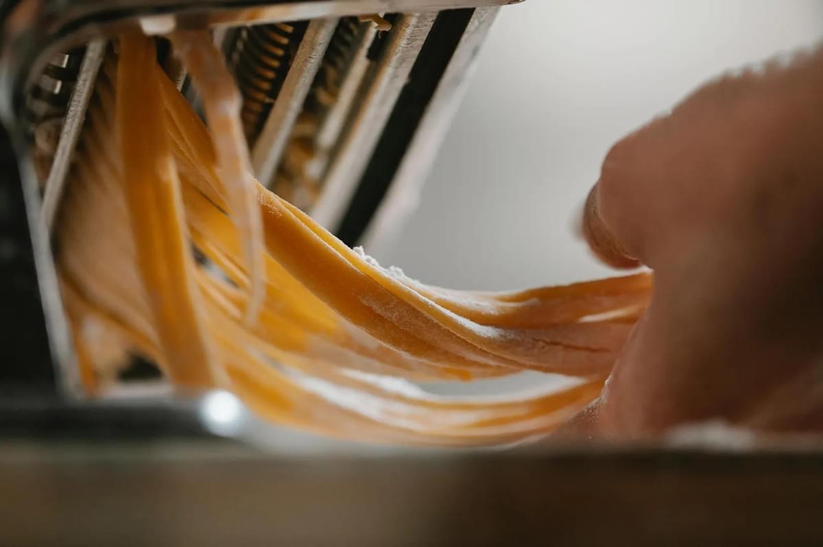 Close-up of fresh pasta dough being cut into strands by a manual pasta machine, dusted with flour. Close-up of fresh pasta dough being cut into strands by a manual pasta machine, dusted with flour.