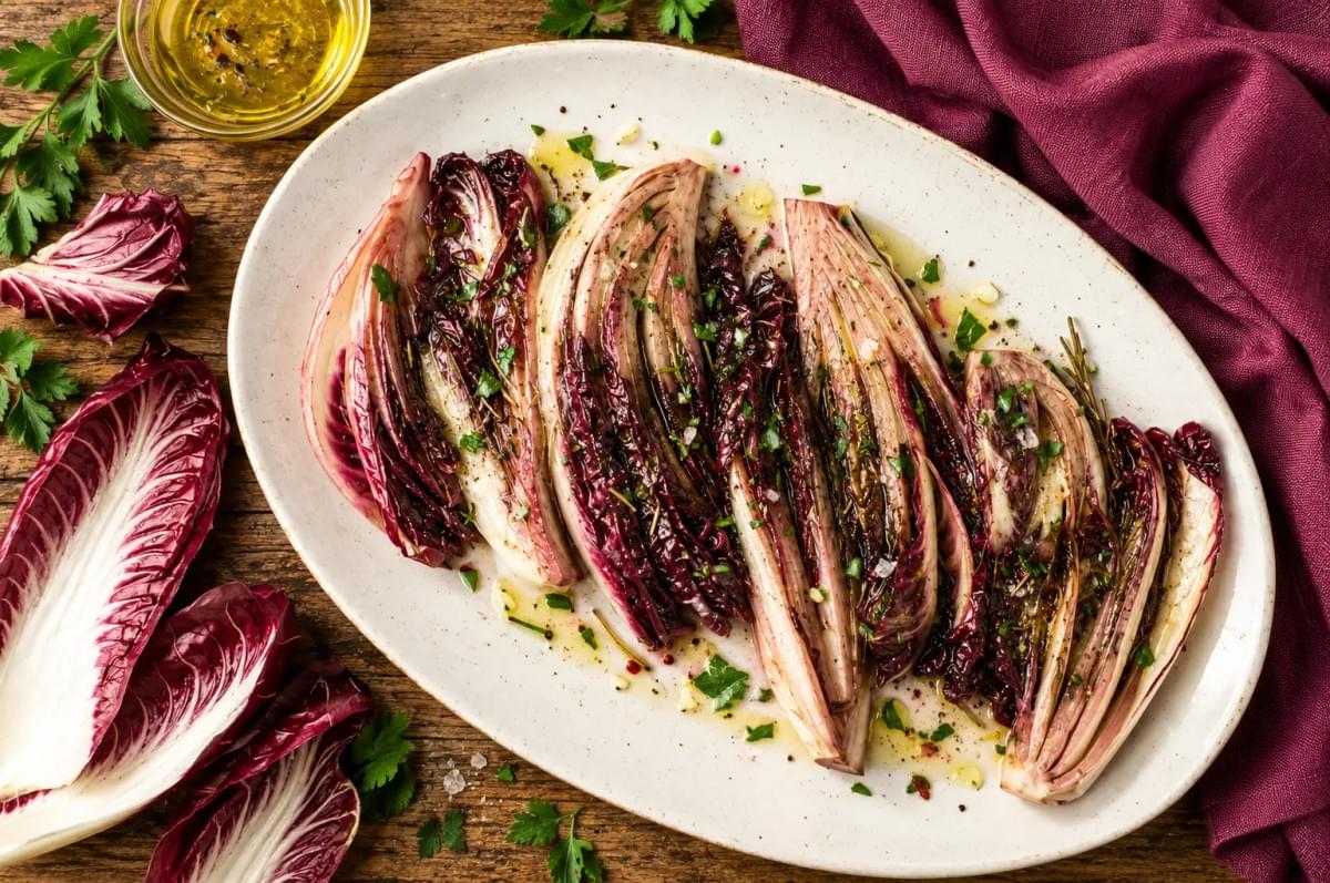 Platter of seared radicchio wedges drizzled with olive oil and herbs on a rustic wooden table. Platter of seared radicchio wedges drizzled with olive oil and herbs on a rustic wooden table.