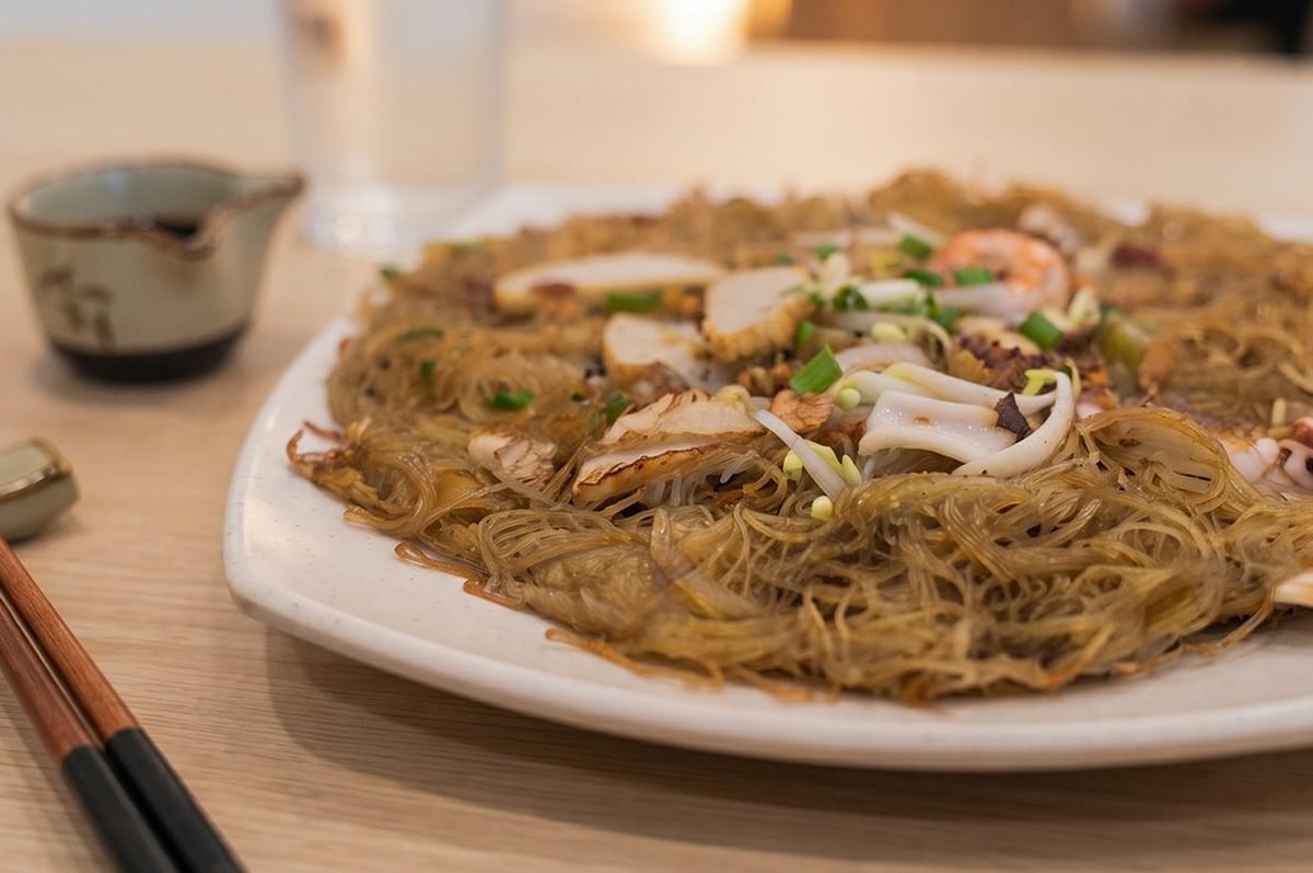 Tang Tea House signature crispy bee hoon topped with seafood and sliced fish cake served on a plate. Tang Tea House signature crispy bee hoon topped with seafood and sliced fish cake served on a plate.