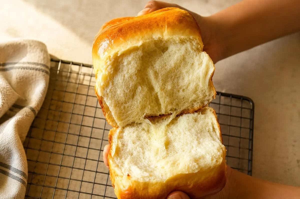 Close-up of hands pulling open a soft loaf of bread to reveal its fluffy texture. Close-up of hands pulling open a soft loaf of bread to reveal its fluffy texture.