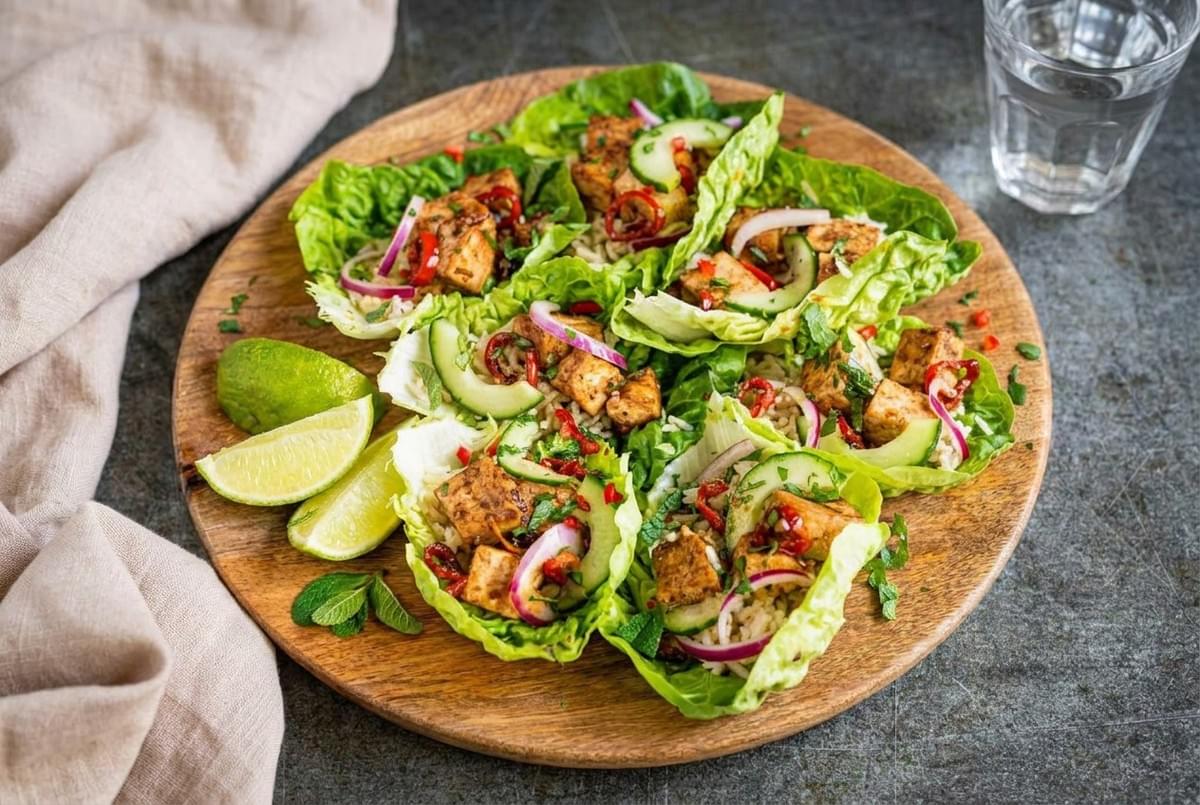 Overhead view of grilled tofu lettuce wraps garnished with sliced cucumber, red onion, and lime wedges. Overhead view of grilled tofu lettuce wraps garnished with sliced cucumber, red onion, and lime wedges.