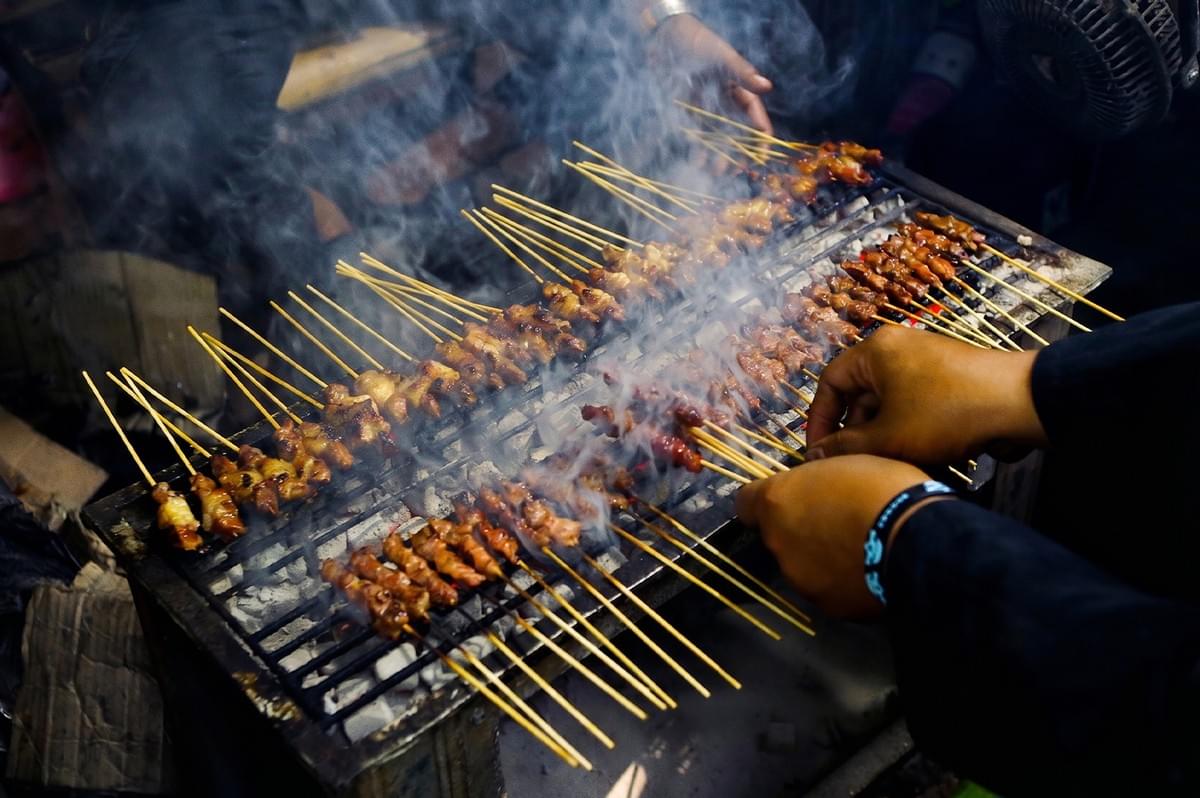 Chicken satay skewers grilling over hot charcoal on a street food grill with thick smoke. Chicken satay skewers grilling over hot charcoal on a street food grill with thick smoke.