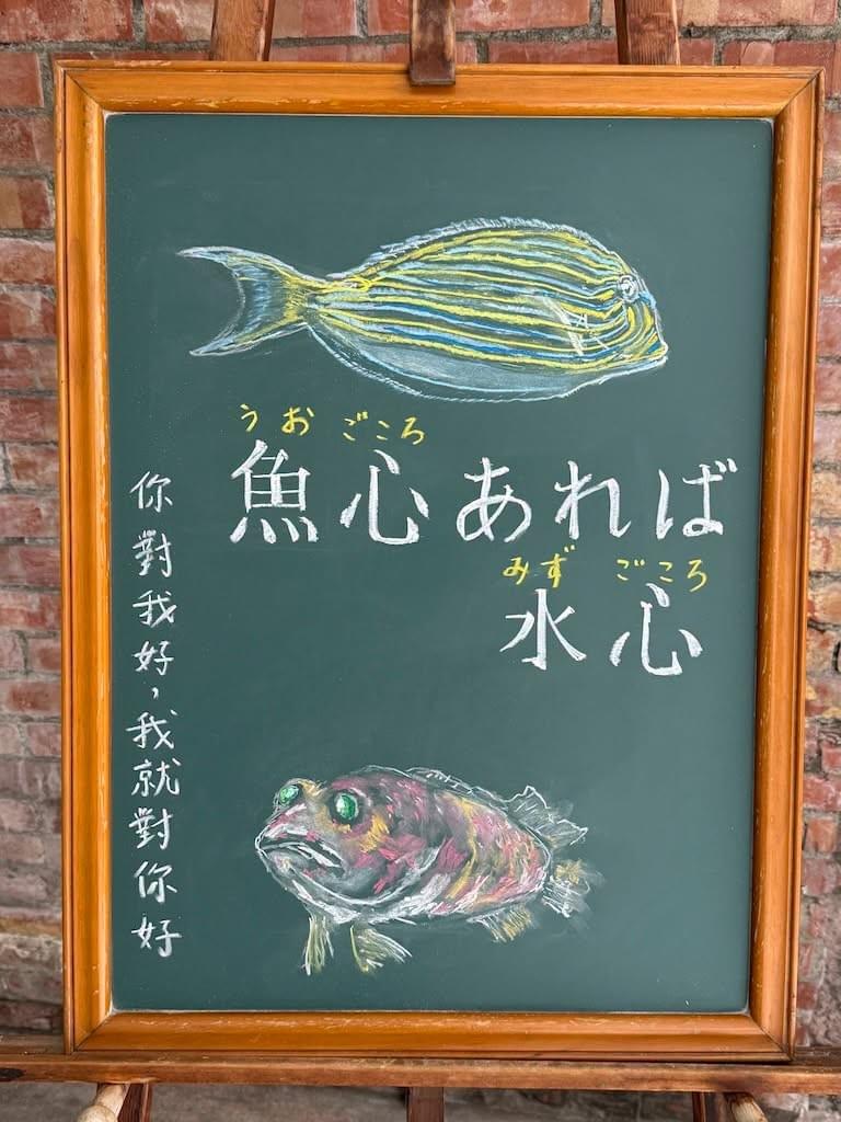 小さい黒板にチョークで絵が描いてあります。日本語のことわざを説明するための黒板です 縦長の黒板で、上部と下部にカラフルな熱帯魚のイラストがあり、中央に横書き二行で「魚心あれば/水心」と書いてあります。 上部の魚は右向きで、黄色と青、黒の細い横縞が何本も入った魚、下部の魚は下部が白、上部に赤い色が入っている魚で、緑色の目が大きくギョロッとしていて、光っています。 どちらの魚も Yutaka Uraki さんのFBの投稿の写真を見て描いたものです。 小さい黒板にチョークで絵が描いてあります。日本語のことわざを説明するための黒板です 縦長の黒板で、上部と下部にカラフルな熱帯魚のイラストがあり、中央に横書き二行で「魚心あれば/水心」と書いてあります。 上部の魚は右向きで、黄色と青、黒の細い横縞が何本も入った魚、下部の魚は下部が白、上部に赤い色が入っている魚で、緑色の目が大きくギョロッとしていて、光っています。 どちらの魚も Yutaka Uraki さんのFBの投稿の写真を見て描いたものです。