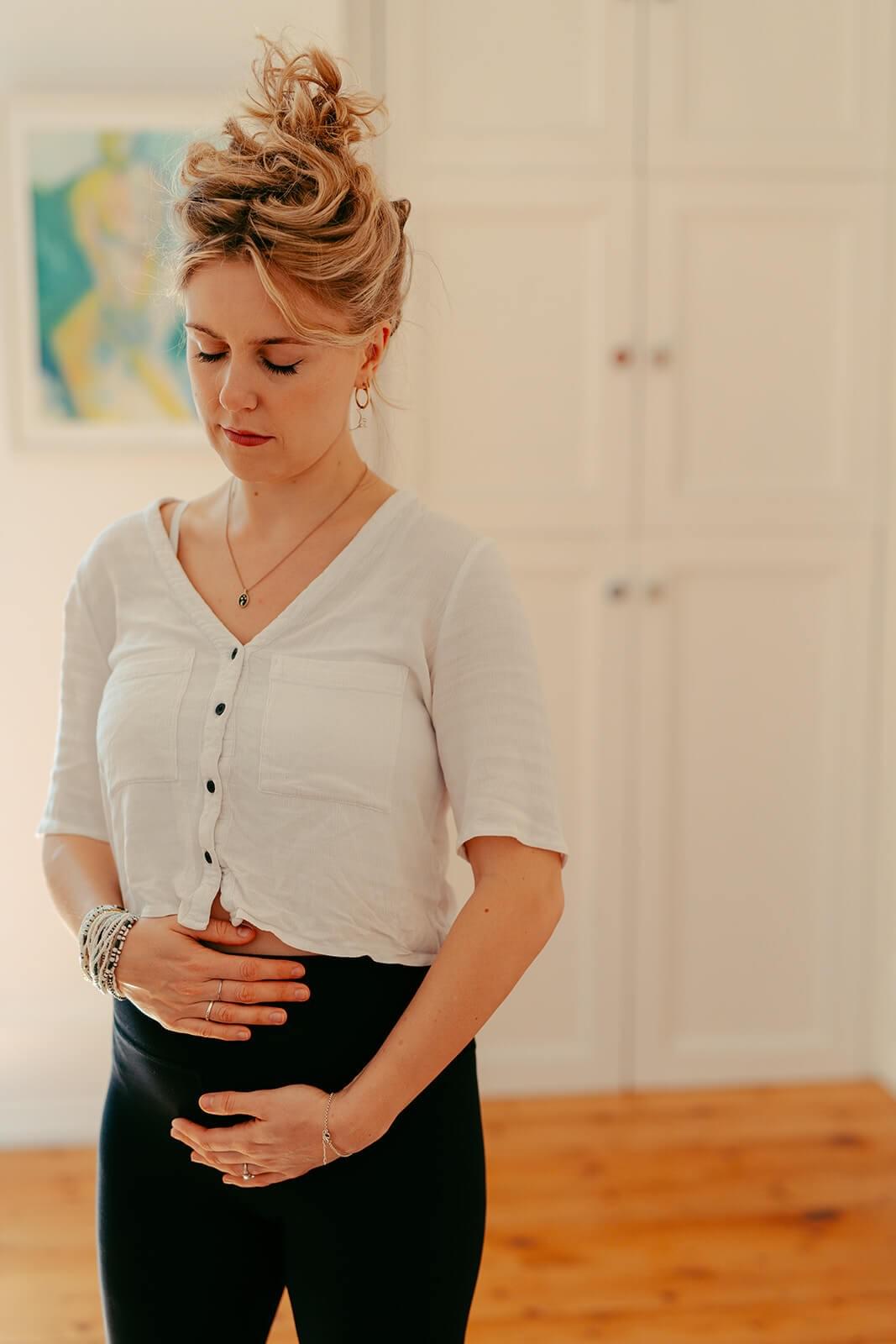 A woman in early pregnancy meditates standing holding her baby bump. A woman in early pregnancy meditates standing holding her baby bump.