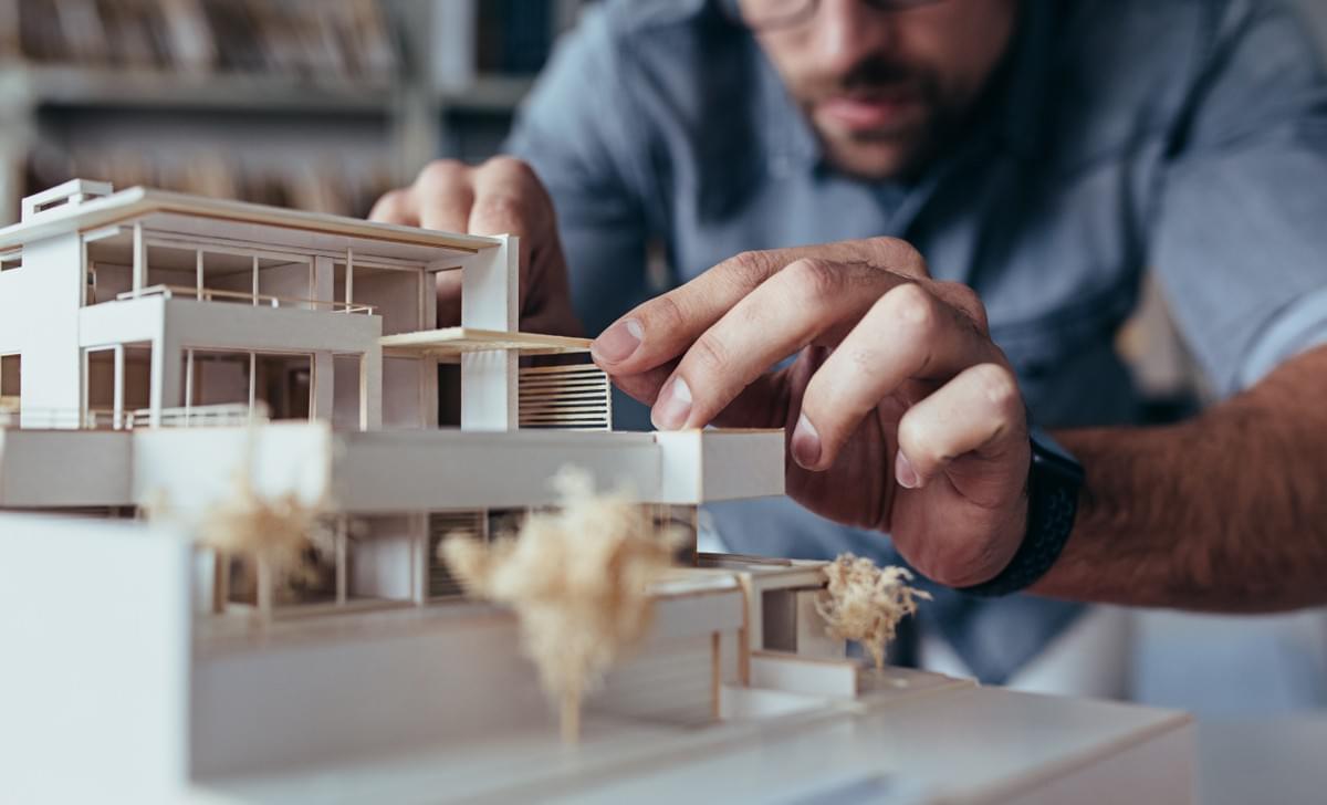 In the context of contract works insurance, a professional person from the construction sector carefully adjusts an architectural model of a contemporary building In the context of contract works insurance, a professional person from the construction sector carefully adjusts an architectural model of a contemporary building