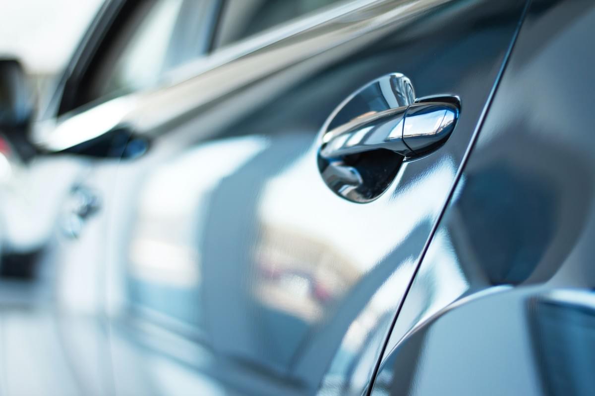 In the context of private motor vehicle insurance, the polished paintwork on the side door of a new car reflects a sunny day In the context of private motor vehicle insurance, the polished paintwork on the side door of a new car reflects a sunny day