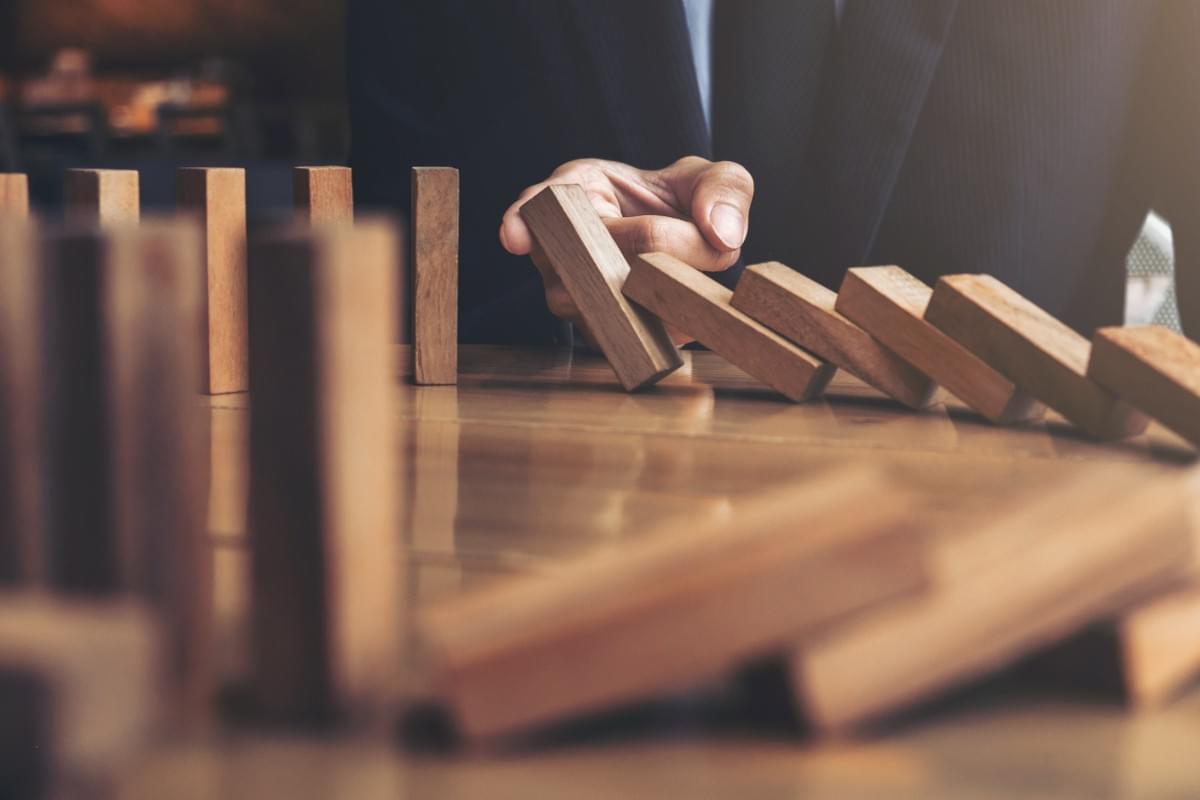 In the context of business interruption insurance, business person places finger between some fallen dominos and those still standing -  to avoid a total collapse In the context of business interruption insurance, business person places finger between some fallen dominos and those still standing -  to avoid a total collapse