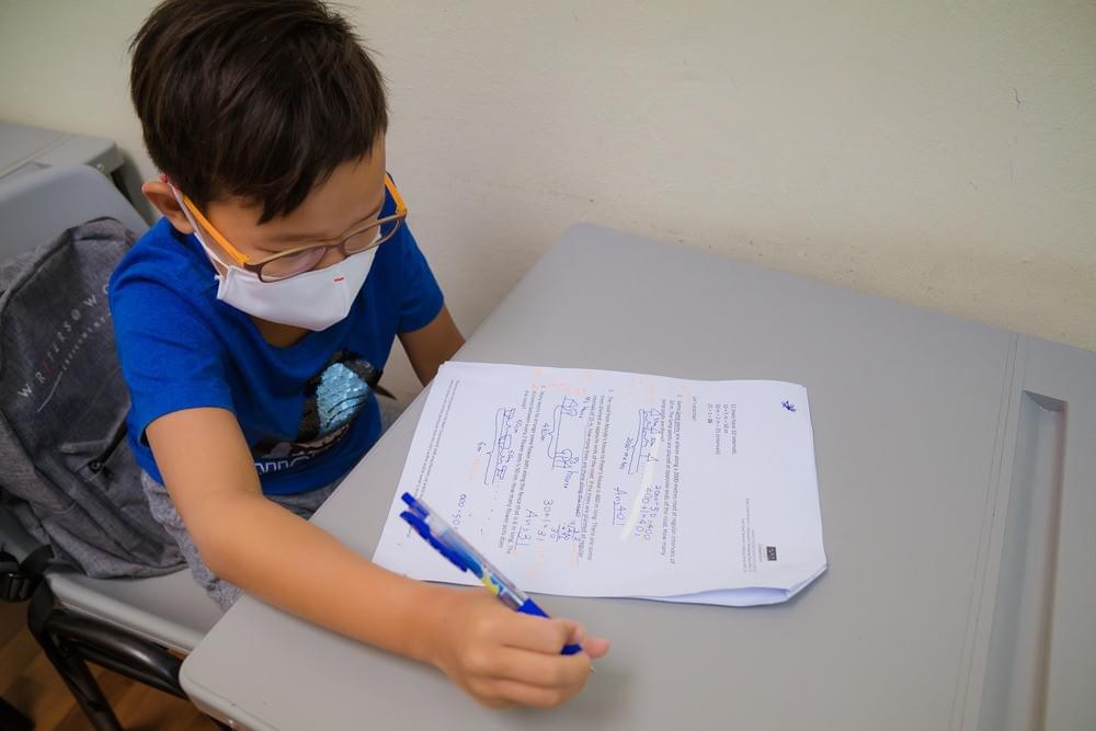 Young student wearing glasses and a face mask completing a primary school mathematics worksheet during a tuition class in Singapore. Young student wearing glasses and a face mask completing a primary school mathematics worksheet during a tuition class in Singapore.