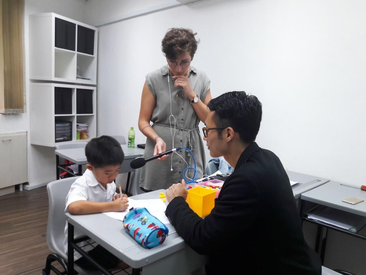A young child participates in an educational assessment or learning activity at a classroom table while writing on paper with a pencil A young child participates in an educational assessment or learning activity at a classroom table while writing on paper with a pencil