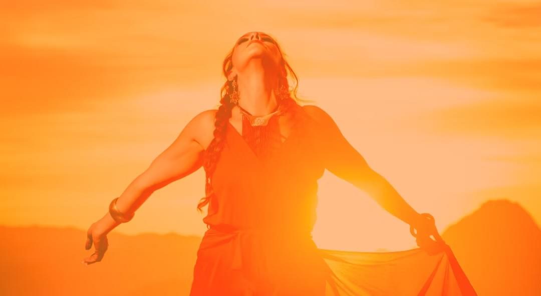 Woman looking up to the sky with her arms outstretched. An orange glow of sunshine behind her. Woman looking up to the sky with her arms outstretched. An orange glow of sunshine behind her.