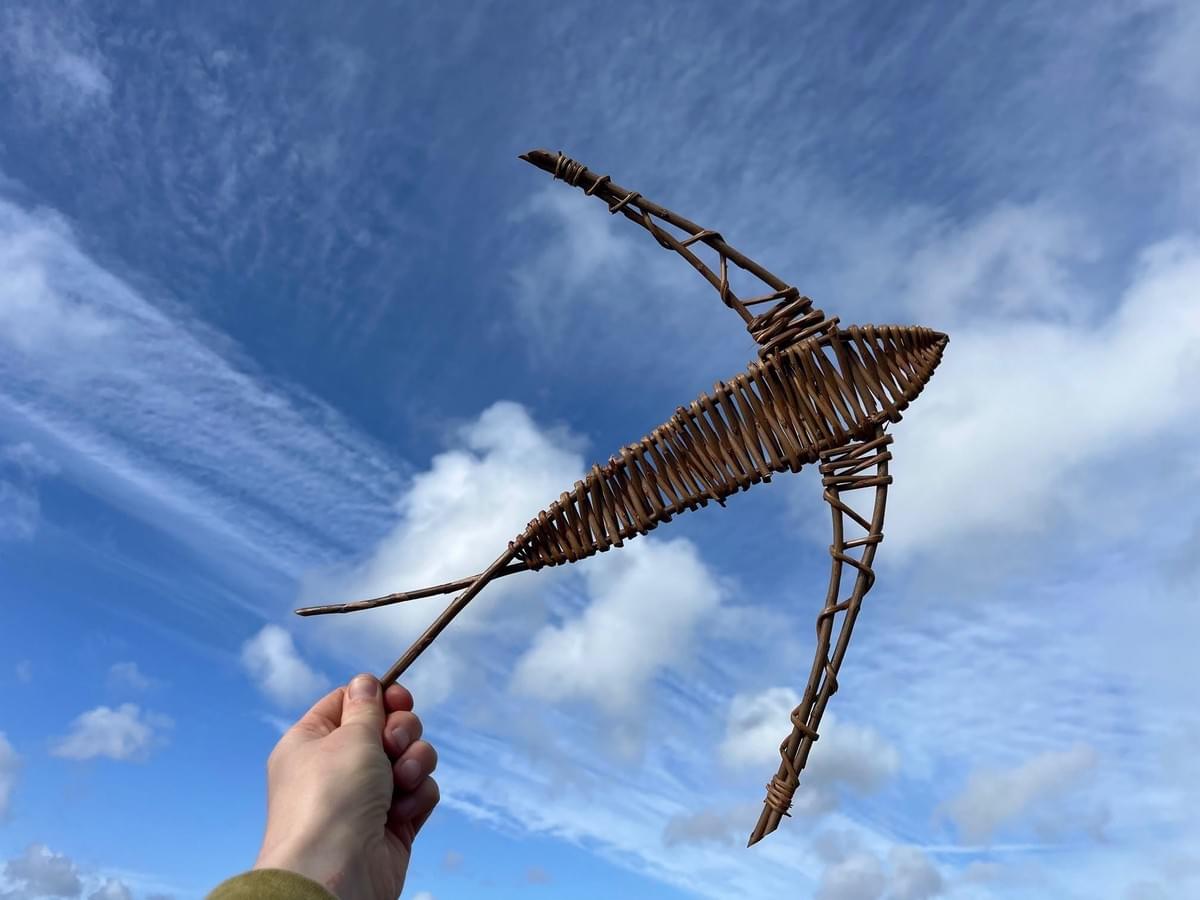 Hand holding up a withy-willow sculpture of a swallow to a background of blue sky and soft fluffy clouds. Hand holding up a withy-willow sculpture of a swallow to a background of blue sky and soft fluffy clouds.
