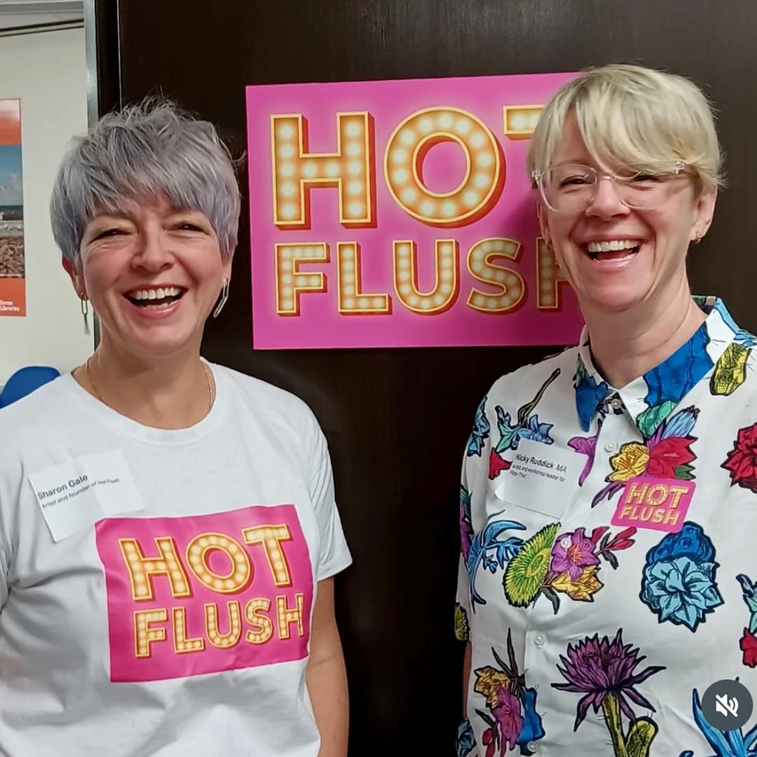 Head to waist shot of two women standing either side of a pink and yellow sign that says Hot Flush. They are facing the camera and laughing  Head to waist shot of two women standing either side of a pink and yellow sign that says Hot Flush. They are facing the camera and laughing