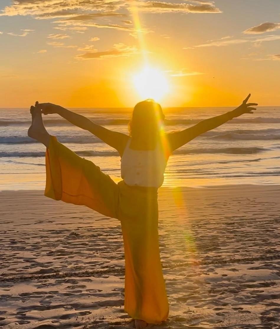 A woman is standing in a yoga pose, on a sandy beach. The sea and golden sunset is behind her. A woman is standing in a yoga pose, on a sandy beach. The sea and golden sunset is behind her.