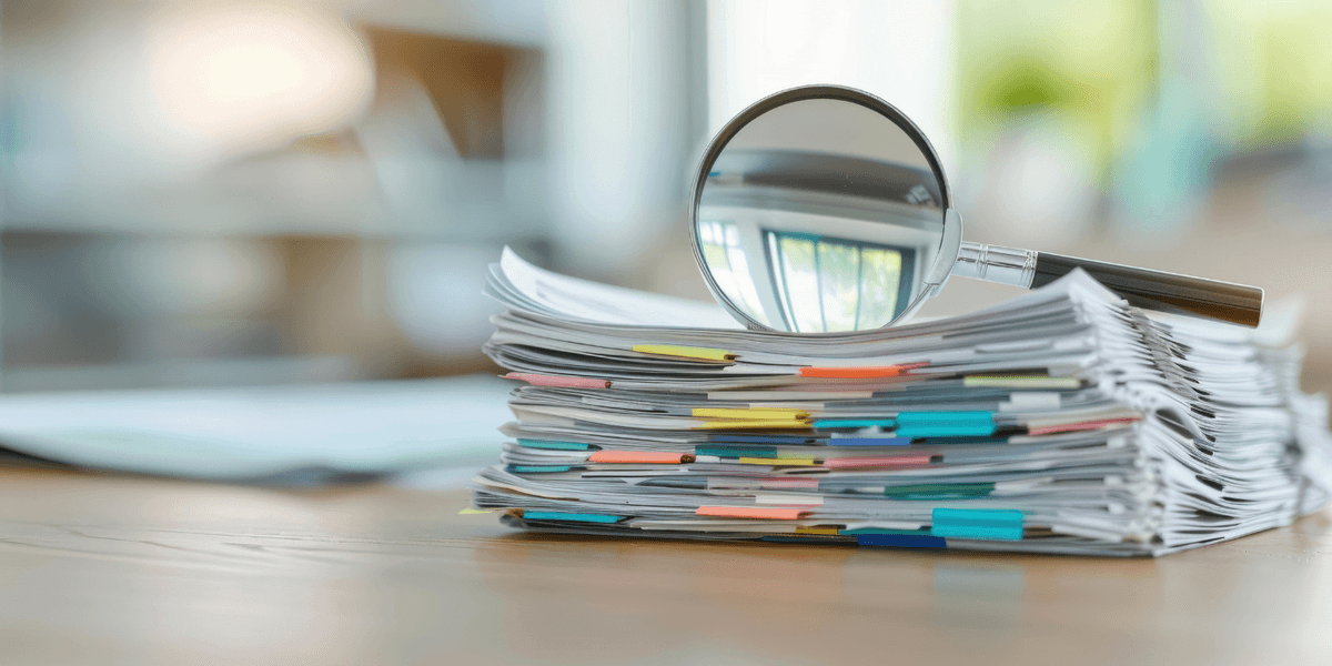 Une loupe est posée sur une grande pile de documents avec des trombones de couleur, sur un bureau en bois. Une loupe est posée sur une grande pile de documents avec des trombones de couleur, sur un bureau en bois.