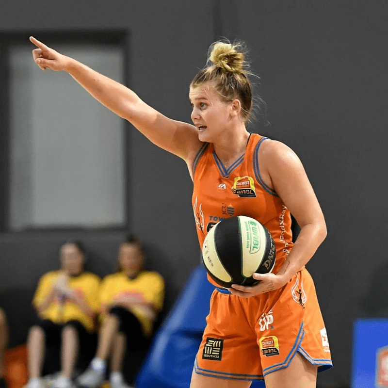 Shyla points while holding the ball in an orange uniform Shyla points while holding the ball in an orange uniform