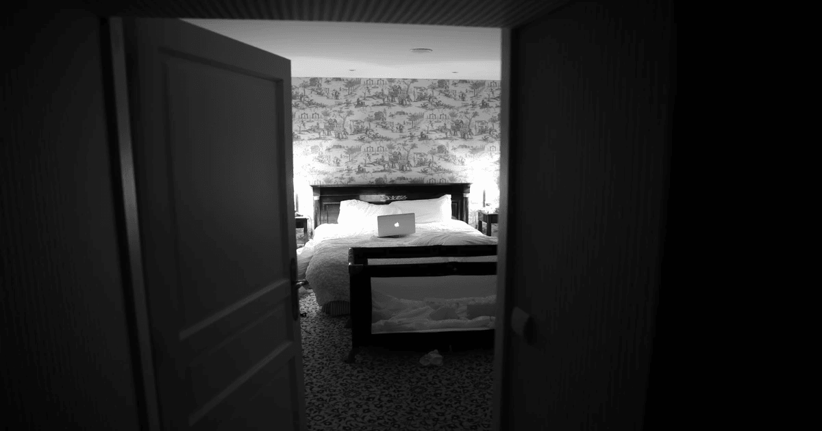 Bedroom door open with MacBook sitting on top of bed with white bed sheets in black and white. Bedroom door open with MacBook sitting on top of bed with white bed sheets in black and white.