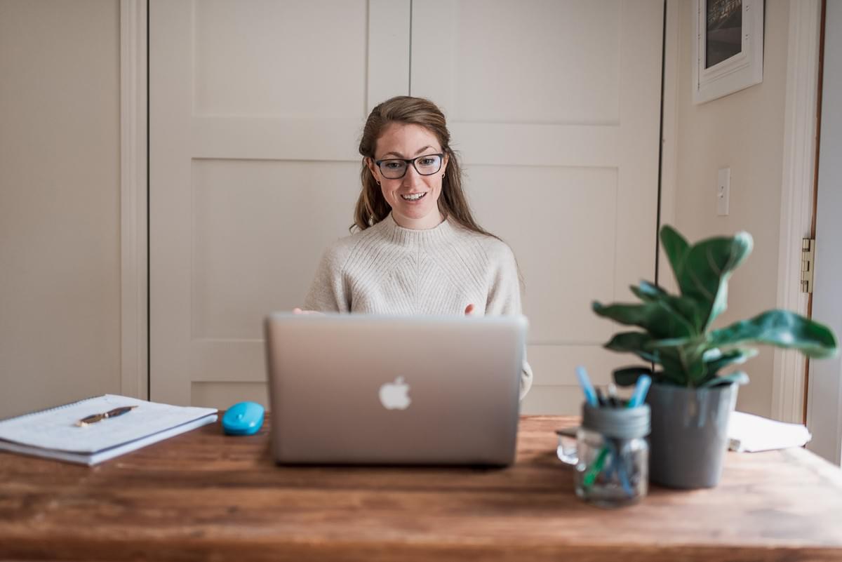 blond woman sitting at a wood desk with blue light glasses on, talking to her computer in a video chat blond woman sitting at a wood desk with blue light glasses on, talking to her computer in a video chat
