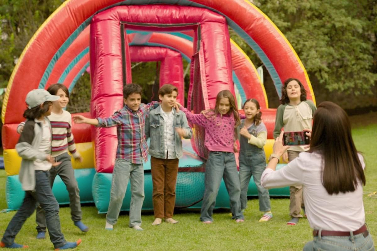 This image shows a group of children playing together in front of a colourful inflatable structure, with one of the adults in the group taking a photo of them. It captures a joyful and lively moment, with the children smiling and interacting in a playful manner. This image shows a group of children playing together in front of a colourful inflatable structure, with one of the adults in the group taking a photo of them. It captures a joyful and lively moment, with the children smiling and interacting in a playful manner.