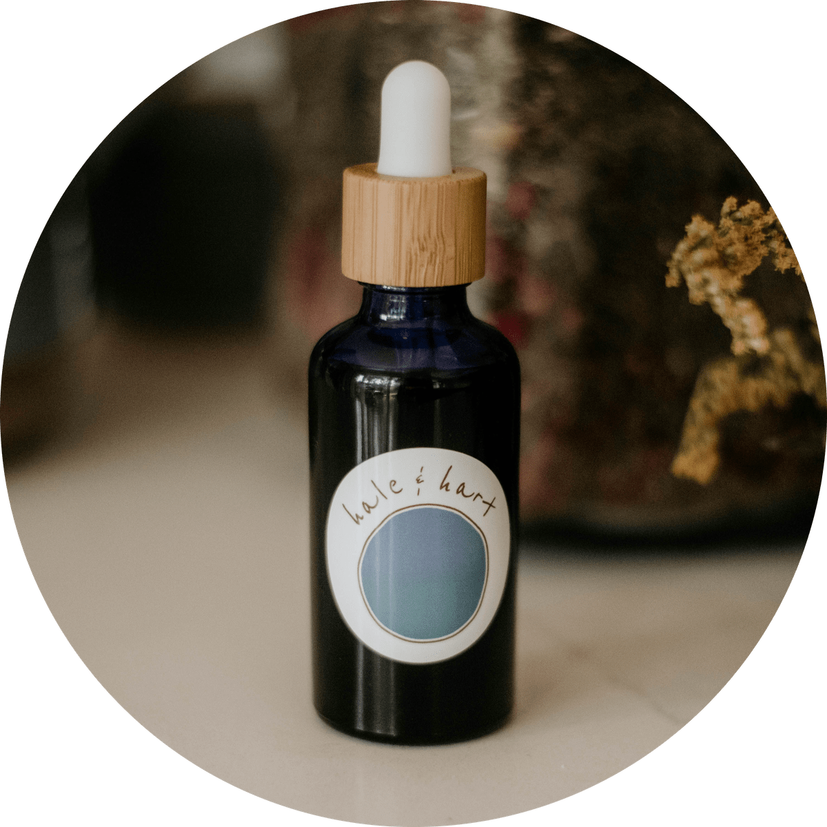 An image of one of Aleksa's custom flower essence blends, made in a blue dropper bottle with a bamboo top. There are herbs in a large glass jar behind on the countertop. An image of one of Aleksa's custom flower essence blends, made in a blue dropper bottle with a bamboo top. There are herbs in a large glass jar behind on the countertop.
