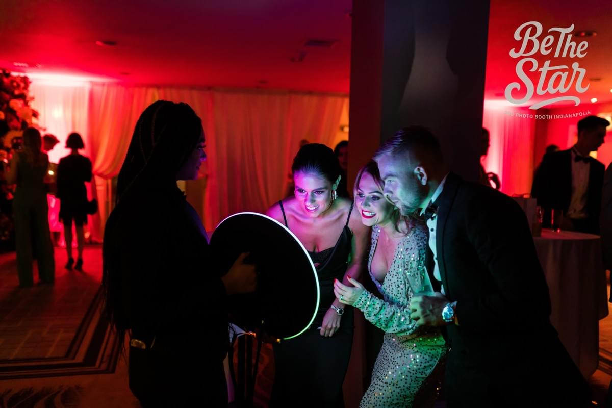 Event guests viewing their photo as an attendant uses a roaming photo booth during a corporate or wedding event. Event guests viewing their photo as an attendant uses a roaming photo booth during a corporate or wedding event.