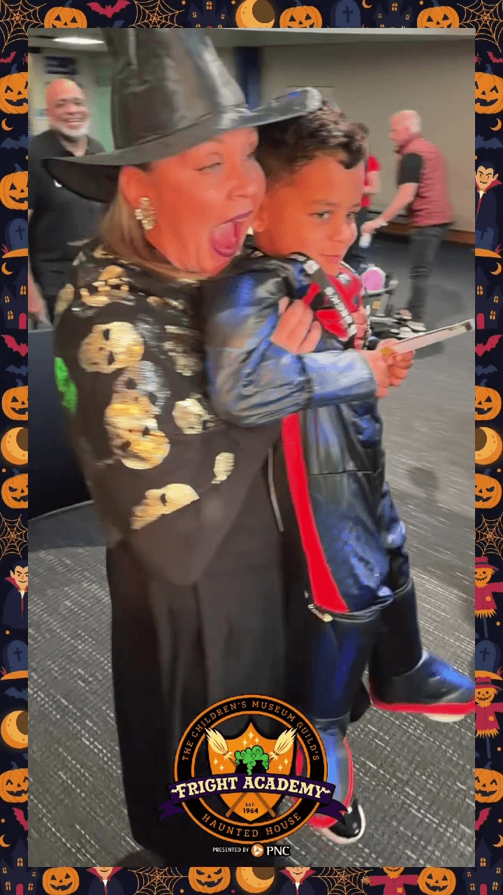 Woman in a black witch hat hugs a boy and laughs at a 360 video booth at a Halloween event Woman in a black witch hat hugs a boy and laughs at a 360 video booth at a Halloween event