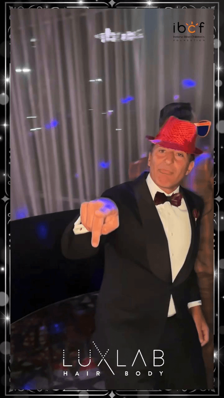 Man in a tuxedo and red sequin hat pointing at the camera at a gala photo booth Man in a tuxedo and red sequin hat pointing at the camera at a gala photo booth