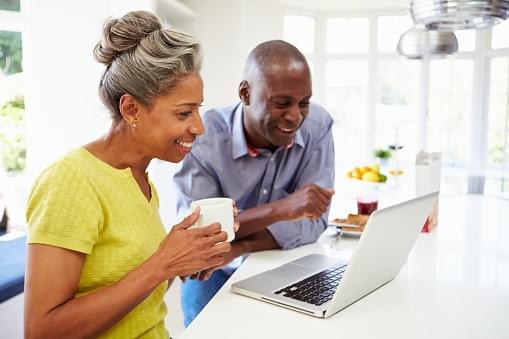 A black couple looking at a computter, the wife has a cup of coffee. A black couple looking at a computter, the wife has a cup of coffee.