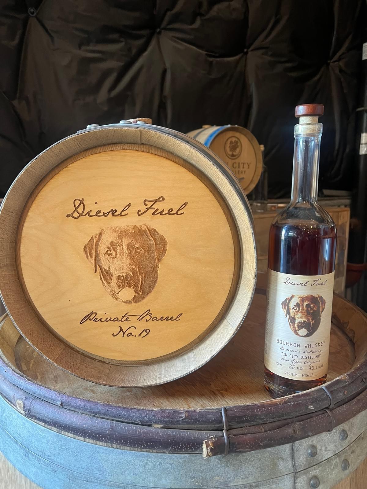 Diesel Fuel private barrel bourbon from Tin City Distillery, shown beside its engraved barrel head with a Labrador portrait and “Private Barrel No. 19” Diesel Fuel private barrel bourbon from Tin City Distillery, shown beside its engraved barrel head with a Labrador portrait and “Private Barrel No. 19”