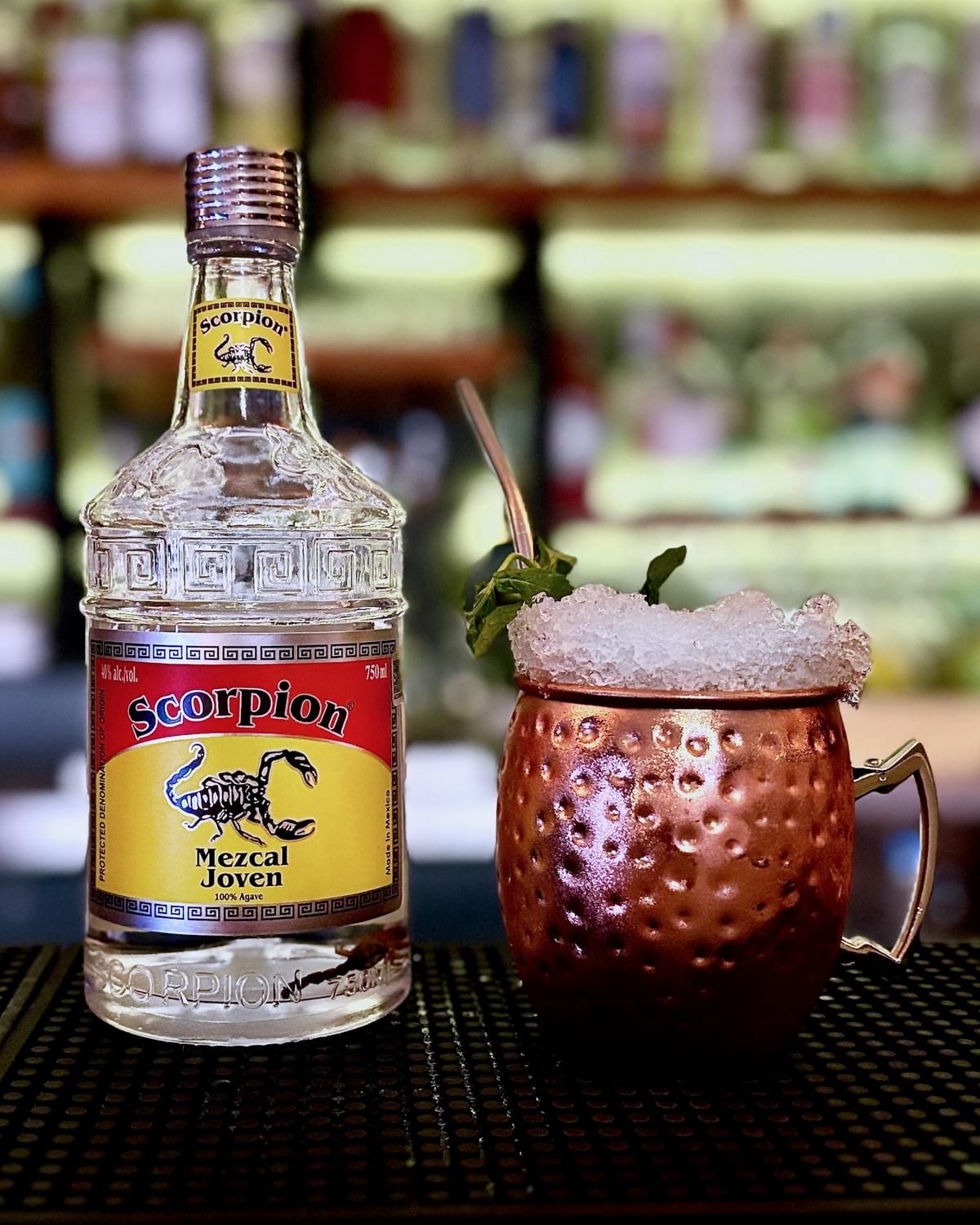 750mL bottle of Scorpion Mezcal Joven and a Mezcal Mule cocktail in a copper mule mug with crushed ice. 750mL bottle of Scorpion Mezcal Joven and a Mezcal Mule cocktail in a copper mule mug with crushed ice.