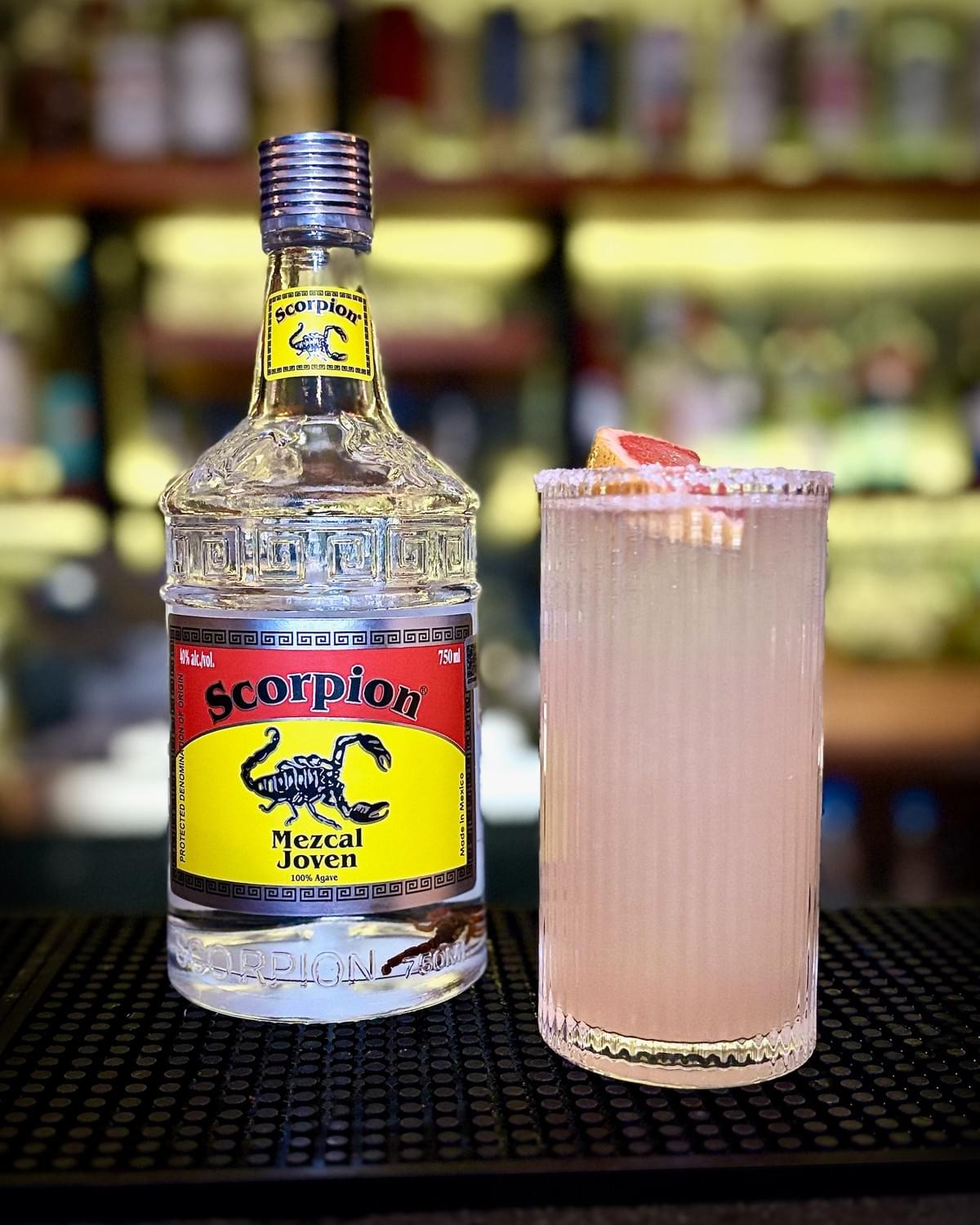 750mL bottle of Scorpion Mezcal Joven and a pink-ish Agave Paloma in a tall cocktail glass. 750mL bottle of Scorpion Mezcal Joven and a pink-ish Agave Paloma in a tall cocktail glass.