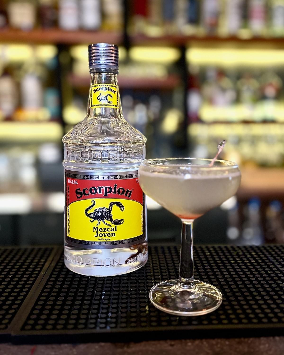 750mL bottle of Scorpion Mezcal Joven and an Ultima Palabra cocktail in a coupe glass. 750mL bottle of Scorpion Mezcal Joven and an Ultima Palabra cocktail in a coupe glass.