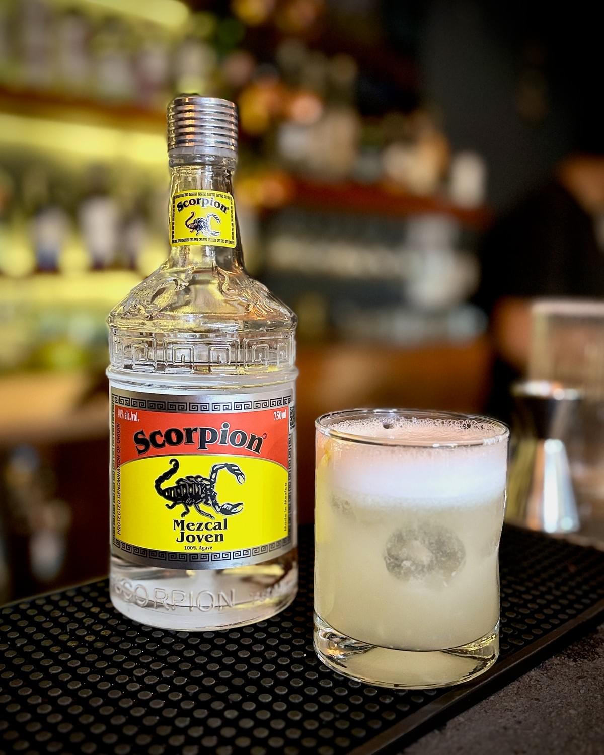 750mL bottle of Scorpion Mezcal Joven and a Vegan Mezcal Sour cocktail in a short cocktail glass. 750mL bottle of Scorpion Mezcal Joven and a Vegan Mezcal Sour cocktail in a short cocktail glass.