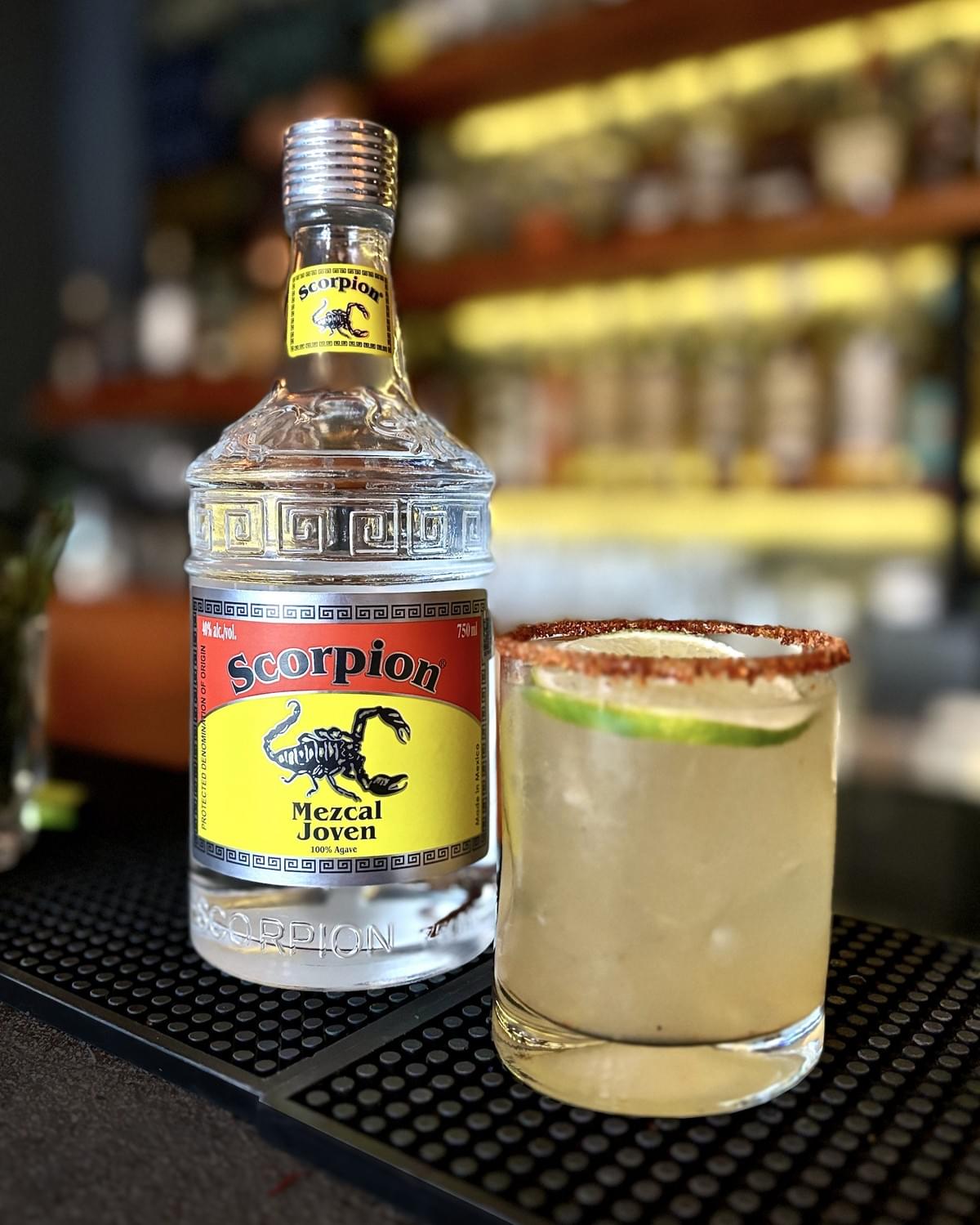 750mL bottle of Scorpion Mezcal Joven and a mezcal margarita with Tajin rim in a short cocktail glass. 750mL bottle of Scorpion Mezcal Joven and a mezcal margarita with Tajin rim in a short cocktail glass.